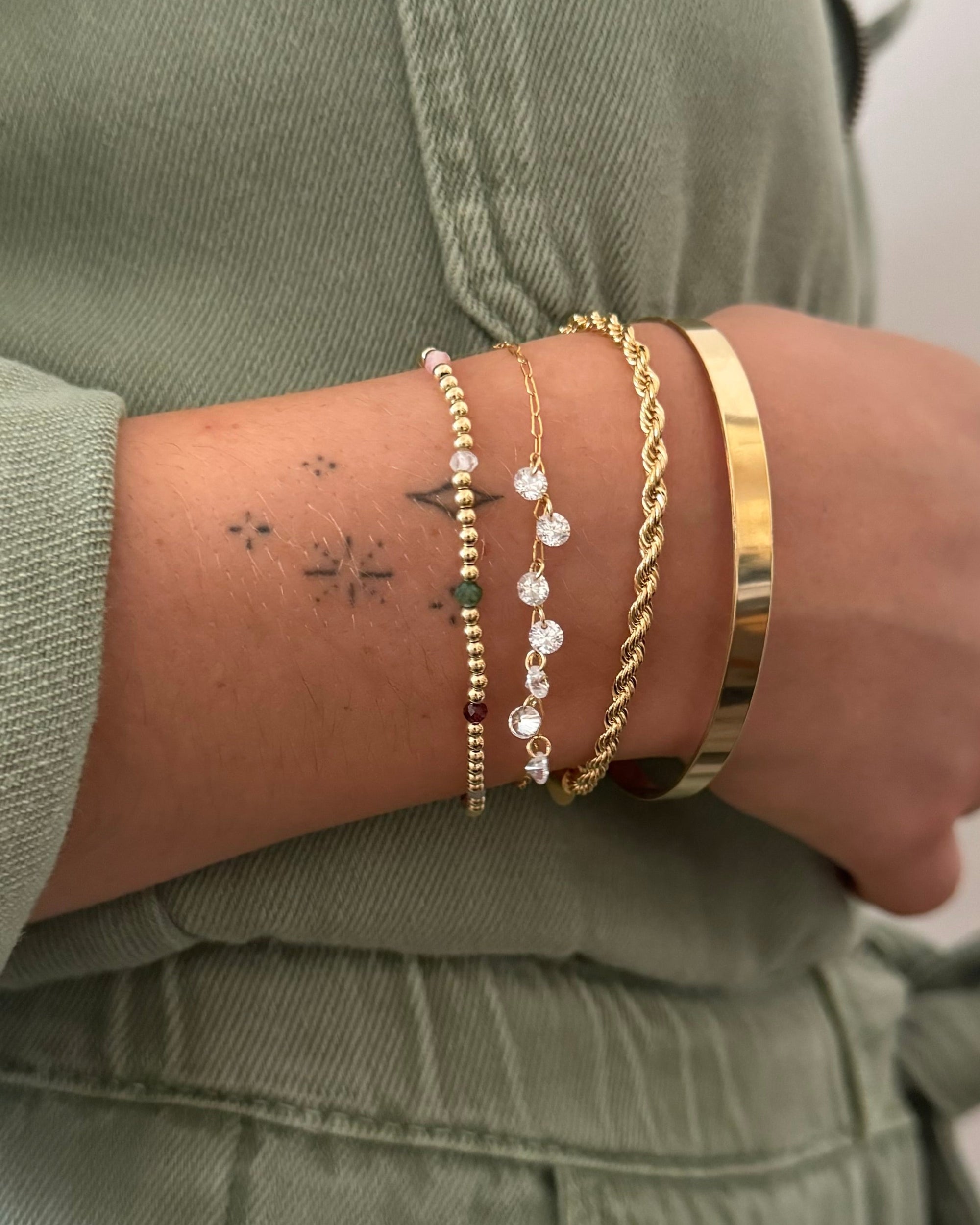 Close-up of a woman's wrist wearing gold bracelets against her green denim jumpsuit