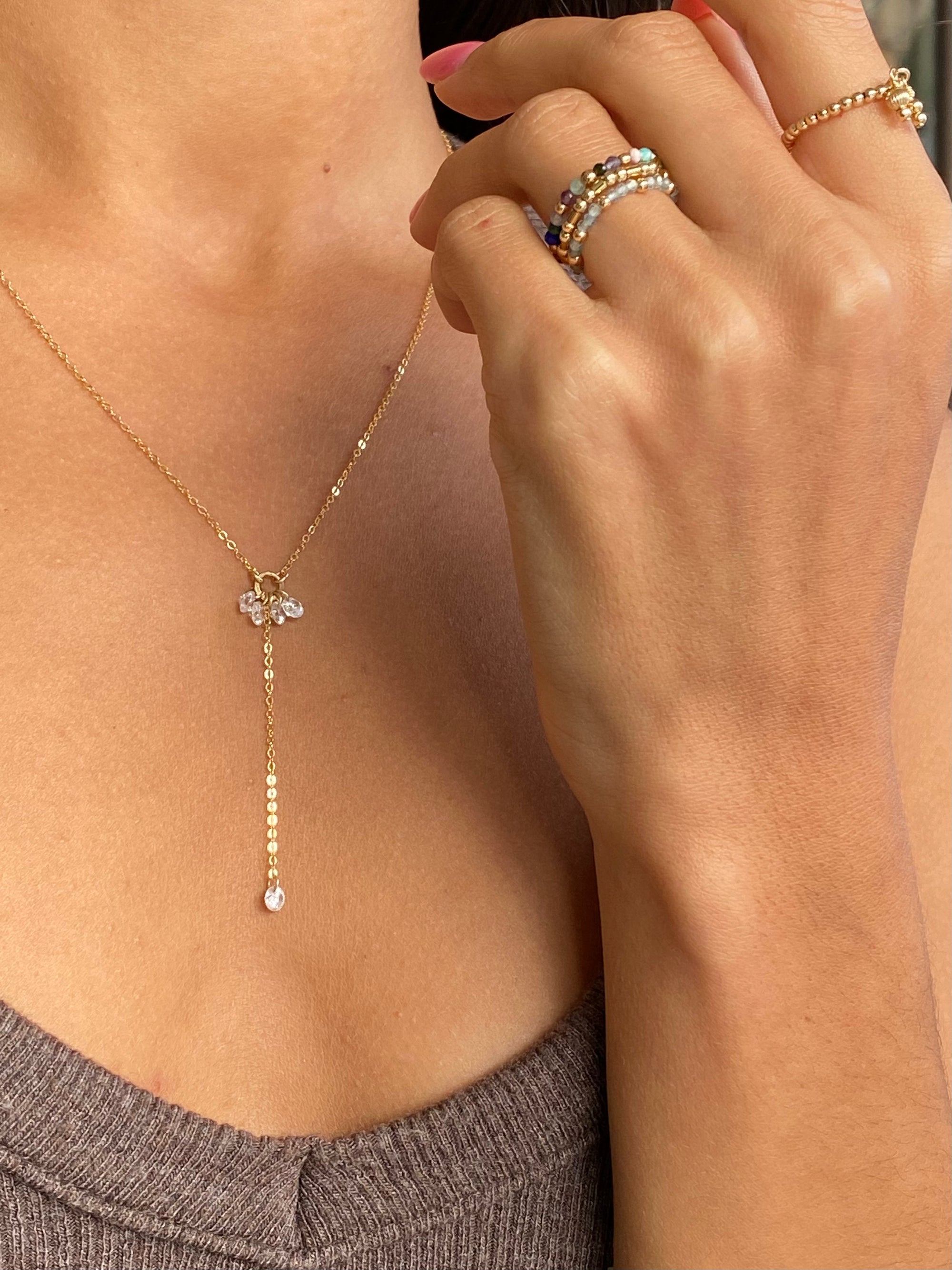 Close up of a woman wearing a gold lariat cubic zirconia necklace and multiple gold beaded and gemstone rings