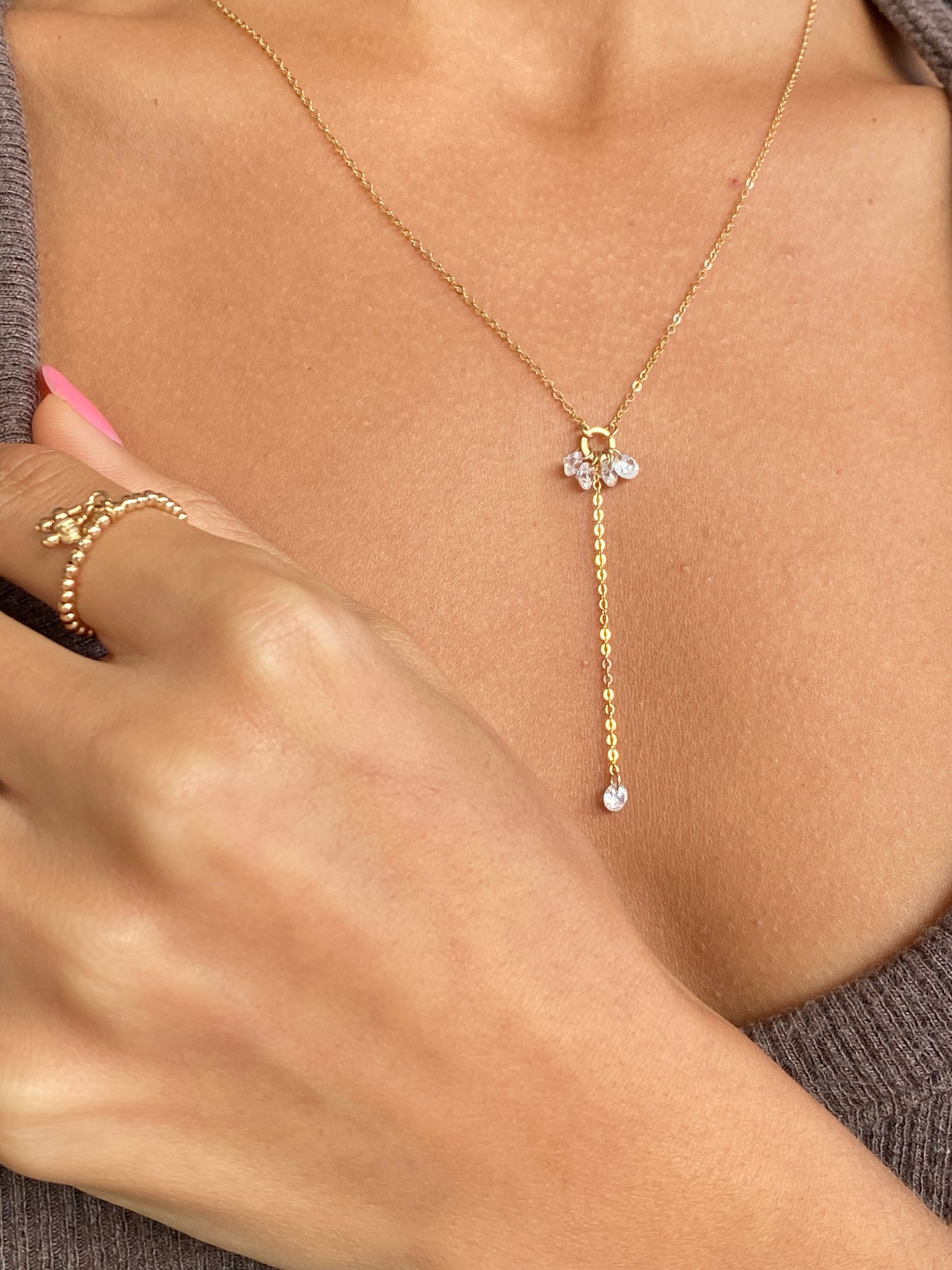 Close up of a woman wearing a gold lariat cubic zirconia necklace and a gold beaded ring