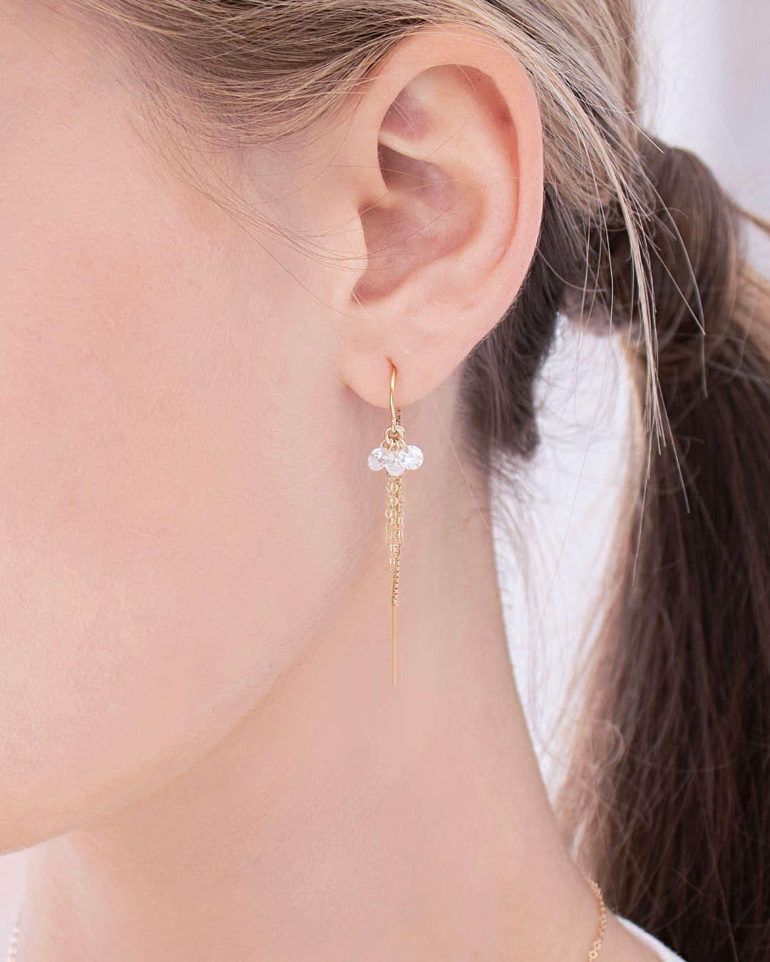 Close-up of a woman's ear wearing a gold cubic zirconia thread earring