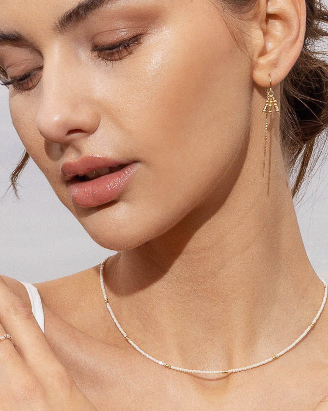 Close-up of a woman wearing a delicate necklace and earring set against a neutral background