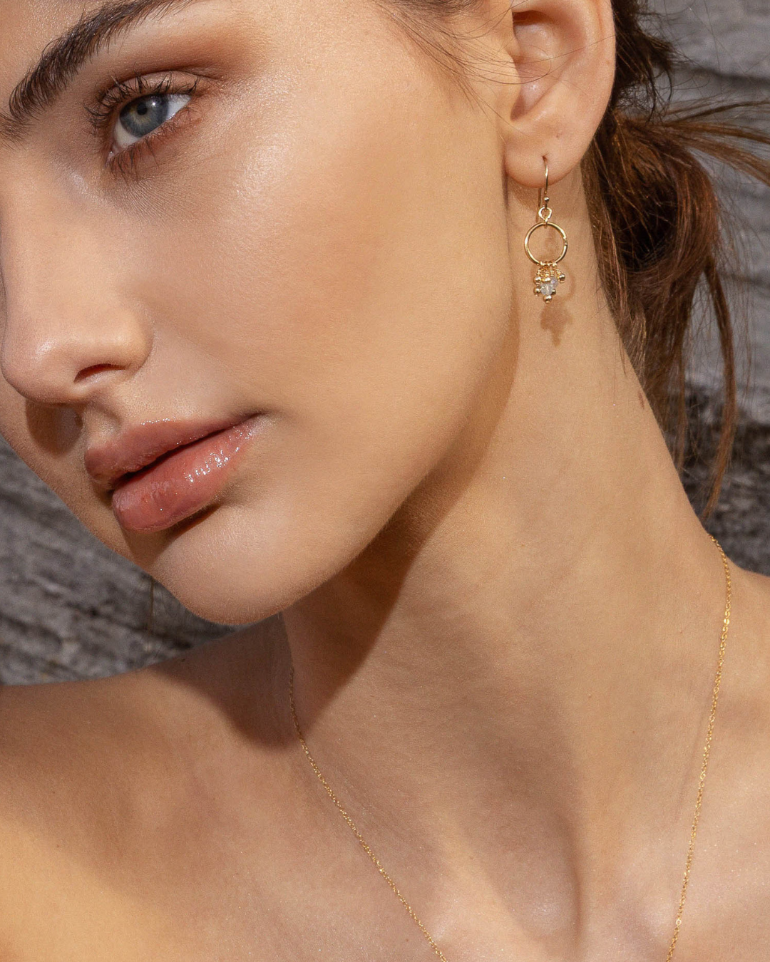 Close-up of a woman wearing gold blue topaz gemstone earrings against a neutral background