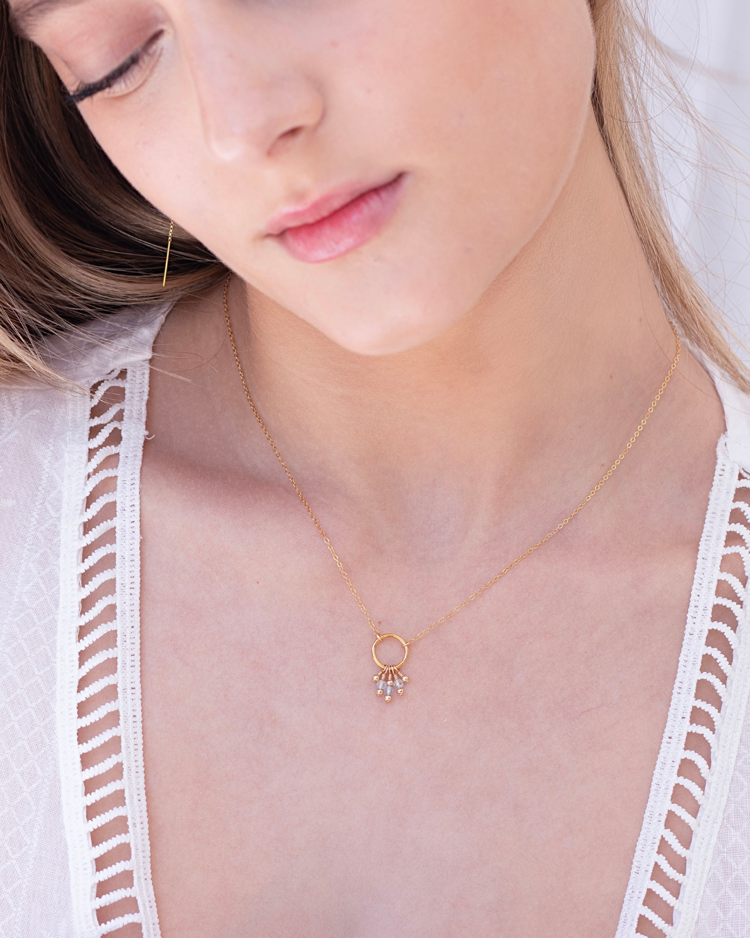 Close-up of a woman wearing a delicate gold blue topaz gemstone necklace wearing a white lace top