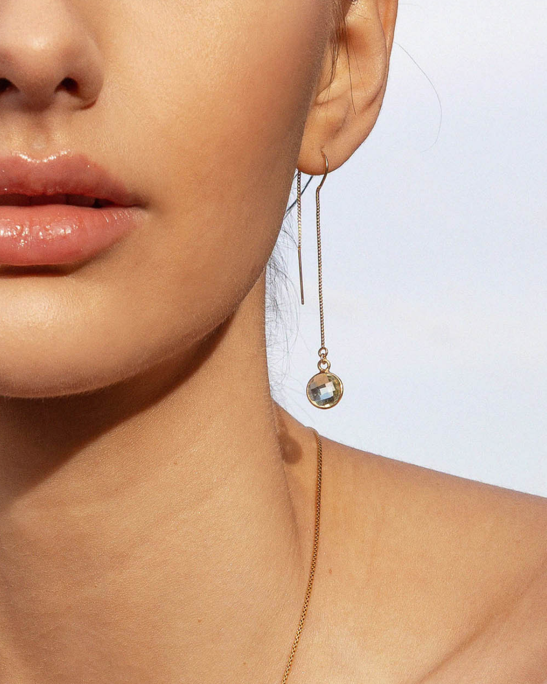 Close-up of a woman wearing a gold green amethyst thread earring