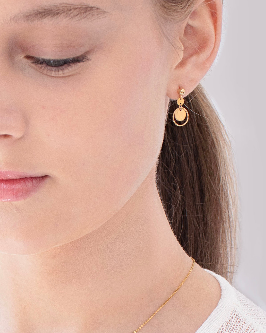 Close-up of a woman wearing a gold earrings and necklace against a neutral background