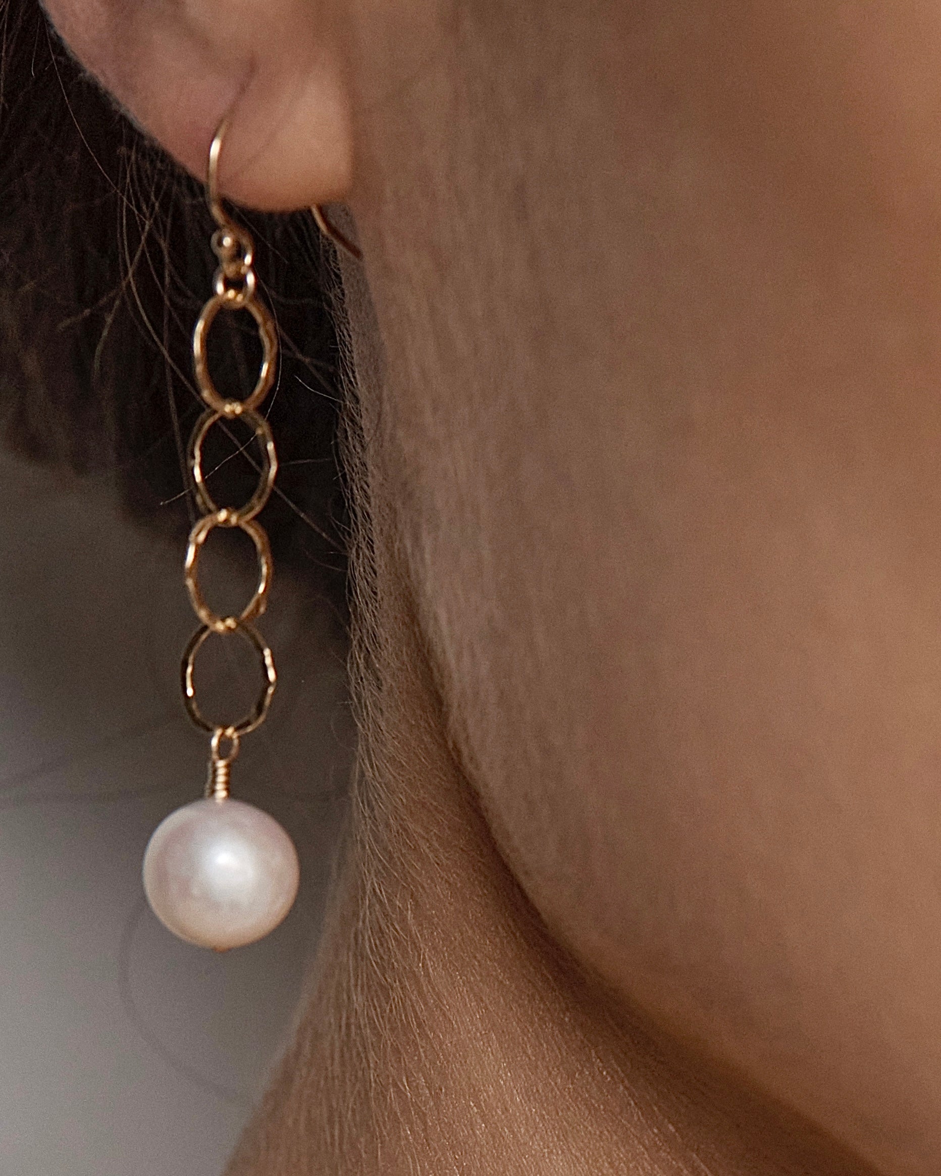 Close-up of a woman's ear wearing a gold chain pearl drop earring