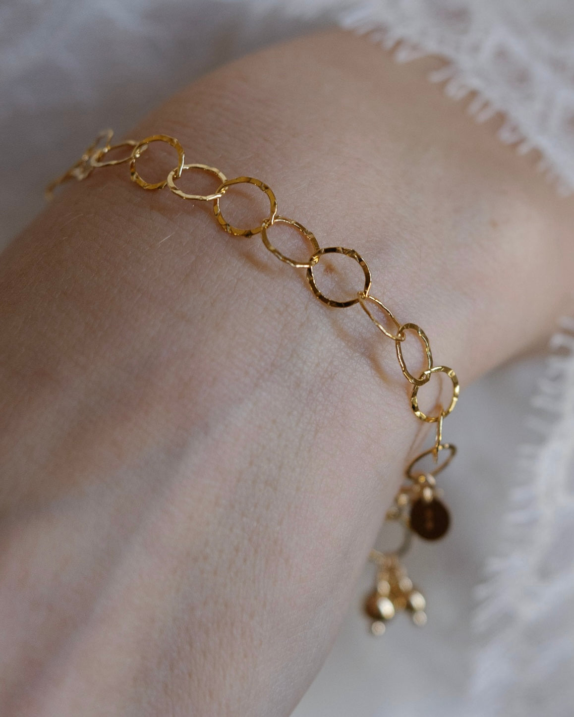 Gold hammered chain bracelet on a wrist against a white lace dress background