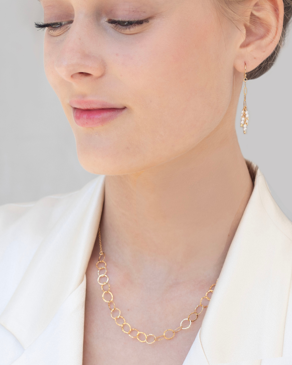 Close-up of a woman wearing a gold pearl earring and a gold chain necklace 