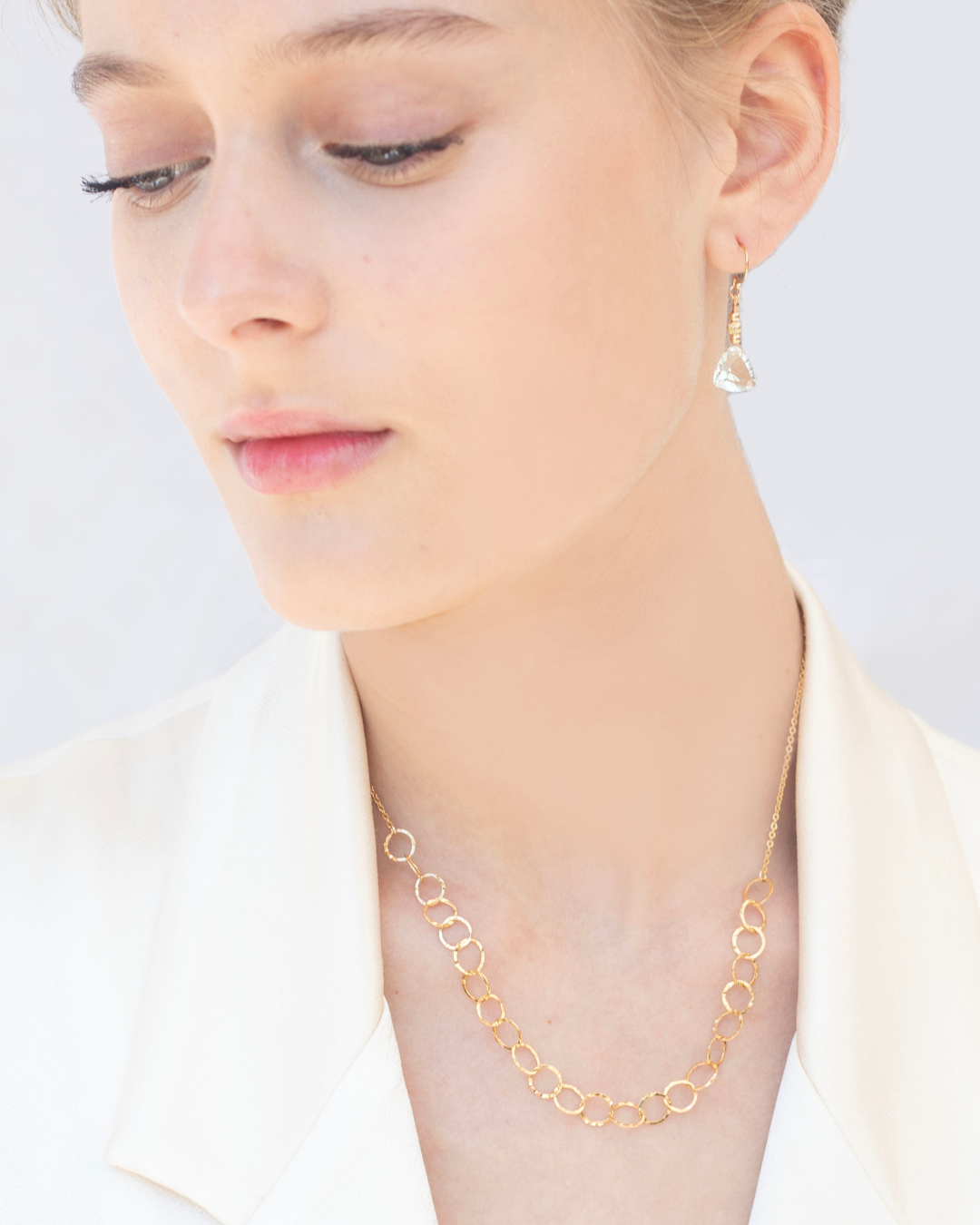 Close-up of a person in a cream satin blazer wearing a gold necklace and green amethyst earrings 