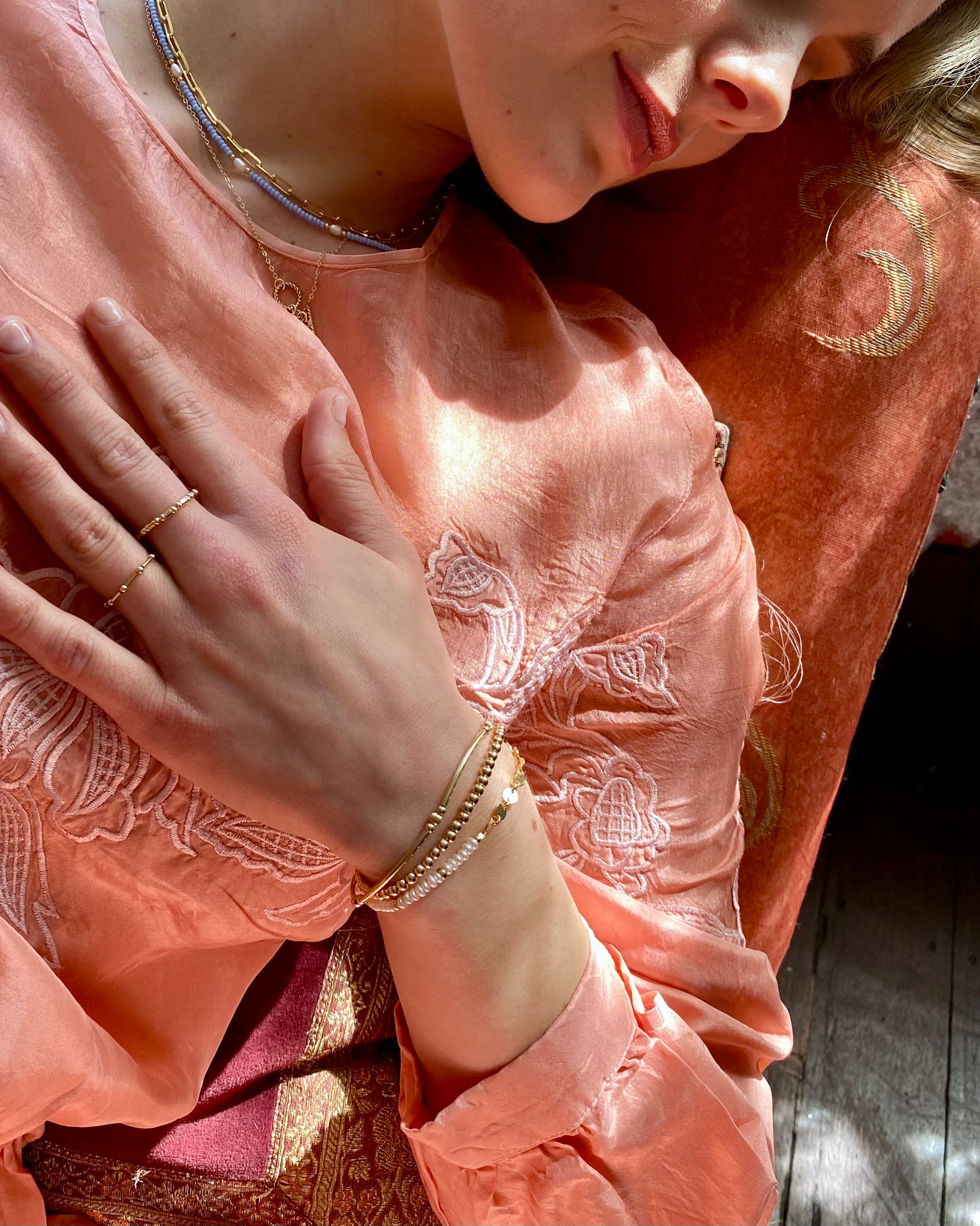 Woman wearing a peach-coloured embroidered dress with gold pearl jewellery.