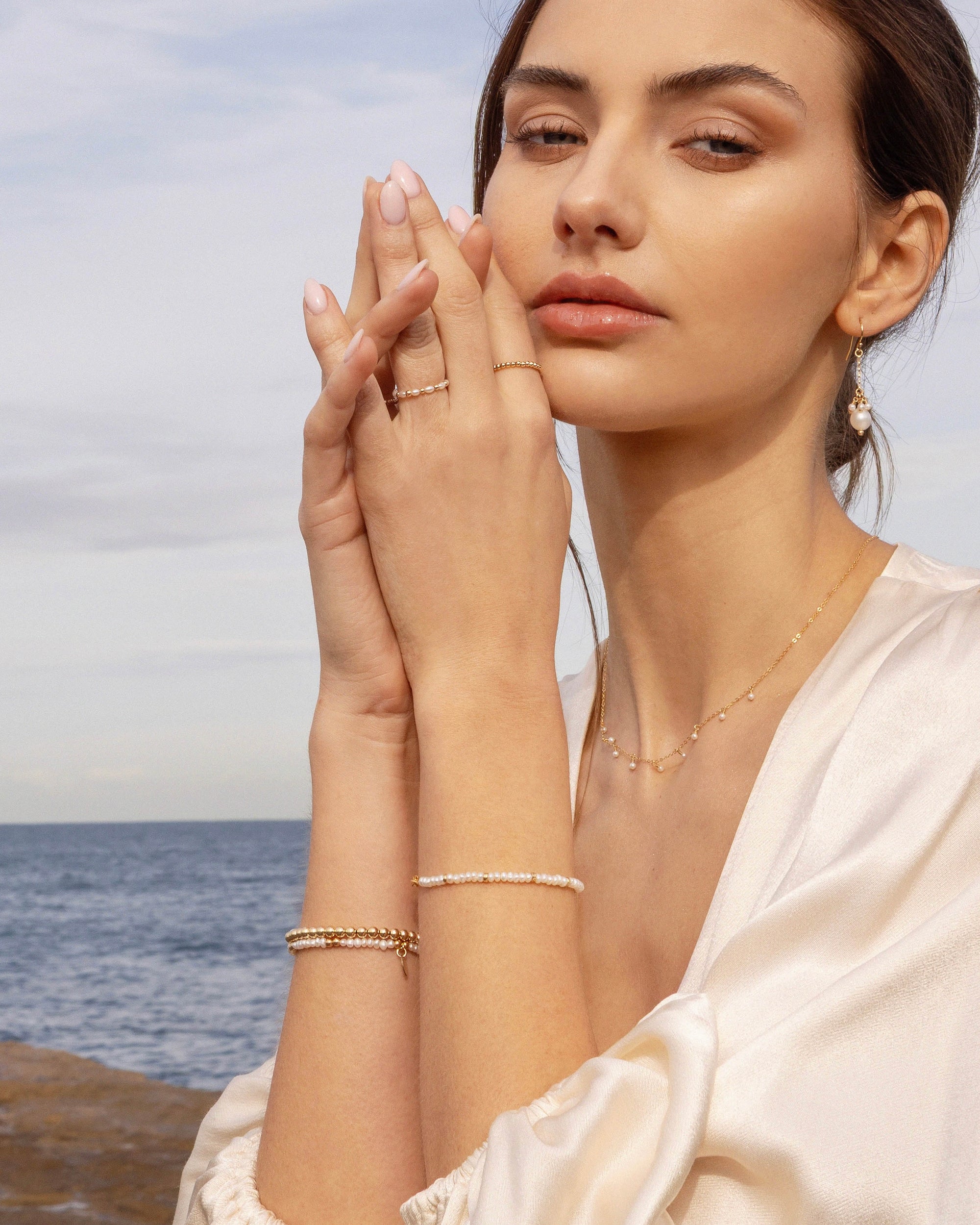 Woman wearing delicate gold pearl jewellery with a blurred beach background