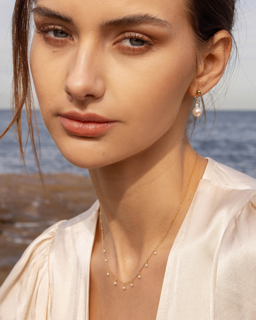 Woman wearing pearl earrings and necklace with ocean in the background