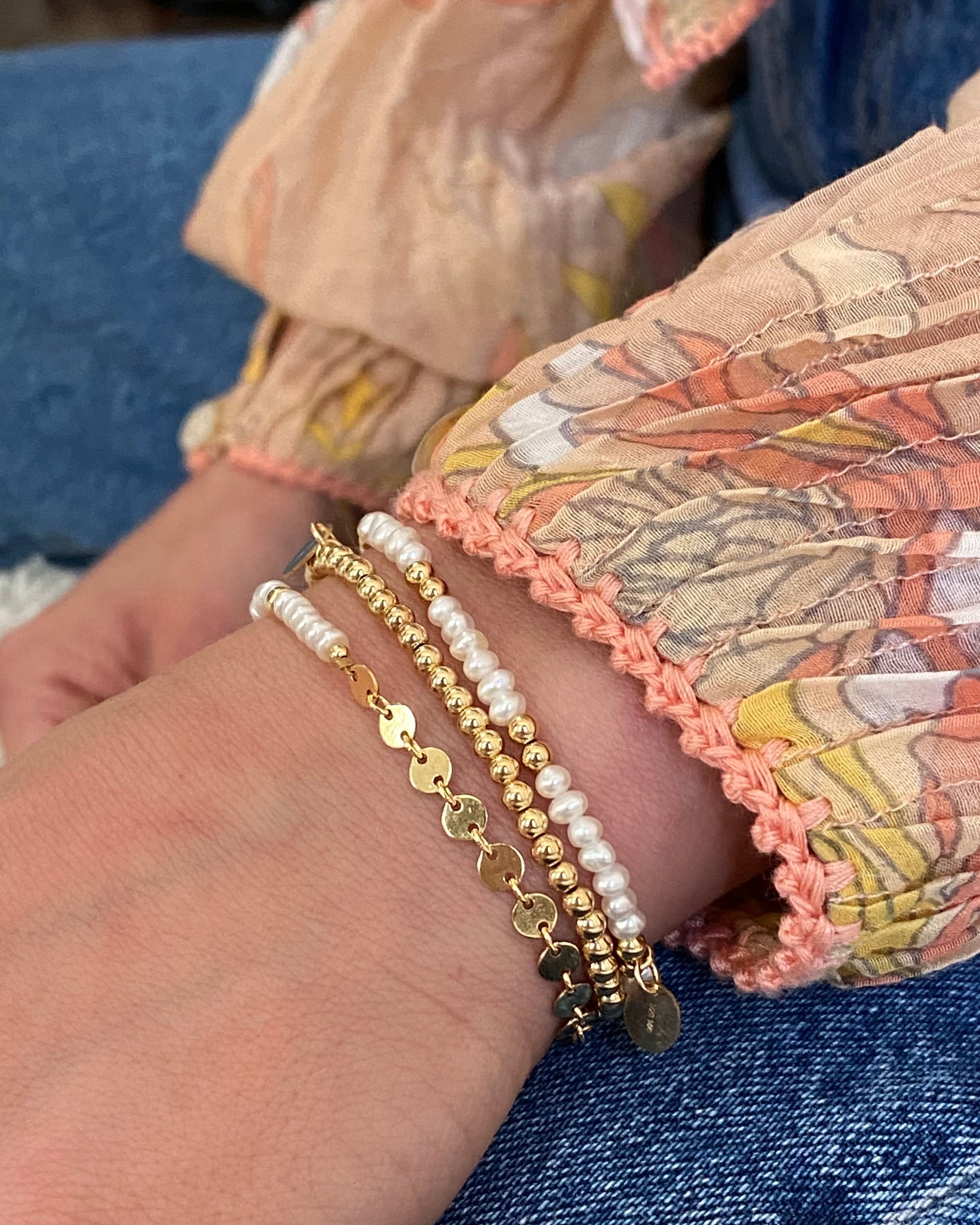 Close-up of a woman's wrist wearing gold and pearl beaded bracelets 