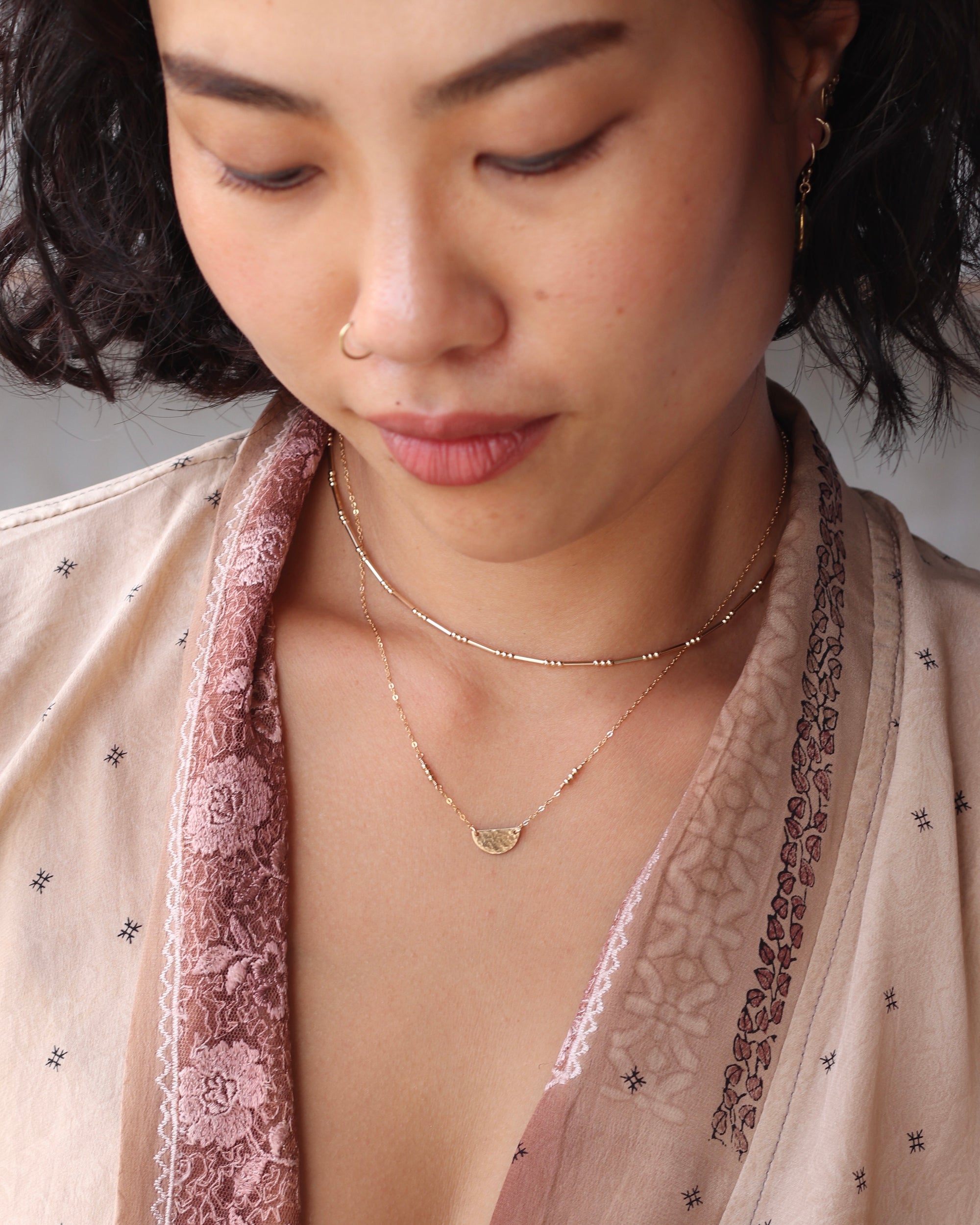 Close-up of a woman wearing delicate necklaces with a nose piercing wearing a silk patterned top.