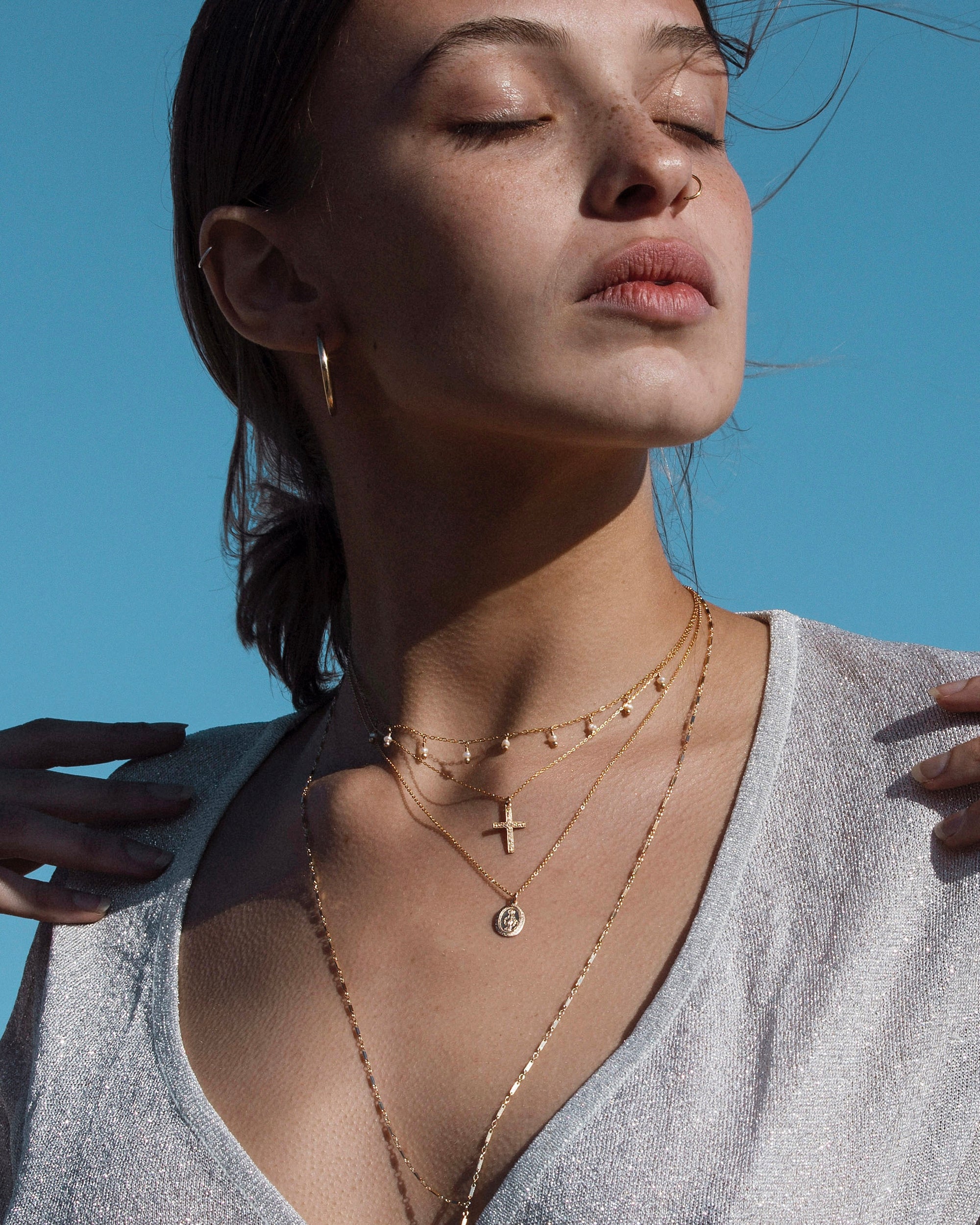 Woman wearing gold religious layered necklaces against a clear blue sky