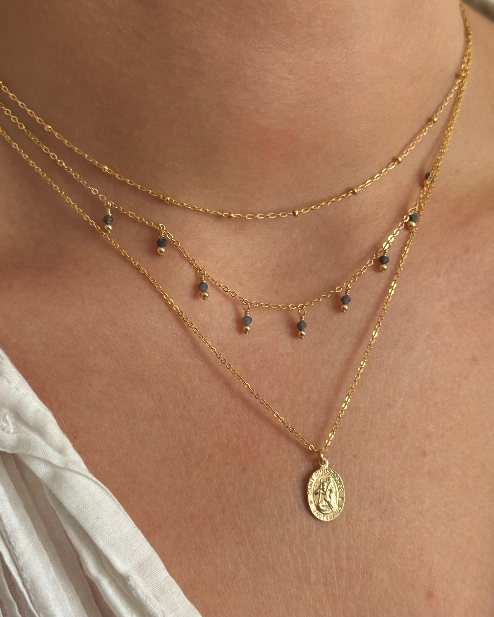 Close-up of a woman's neck wearing layered gold necklaces with a white top.