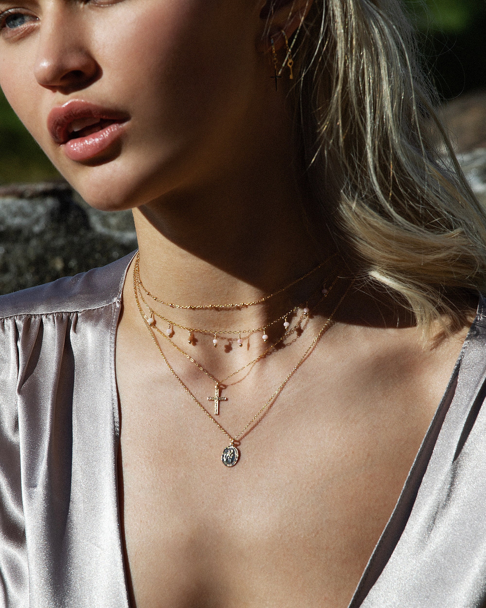 Close-up of a woman wearing a silver top with multiple necklaces layered with a Saint Christopher pendant necklace.