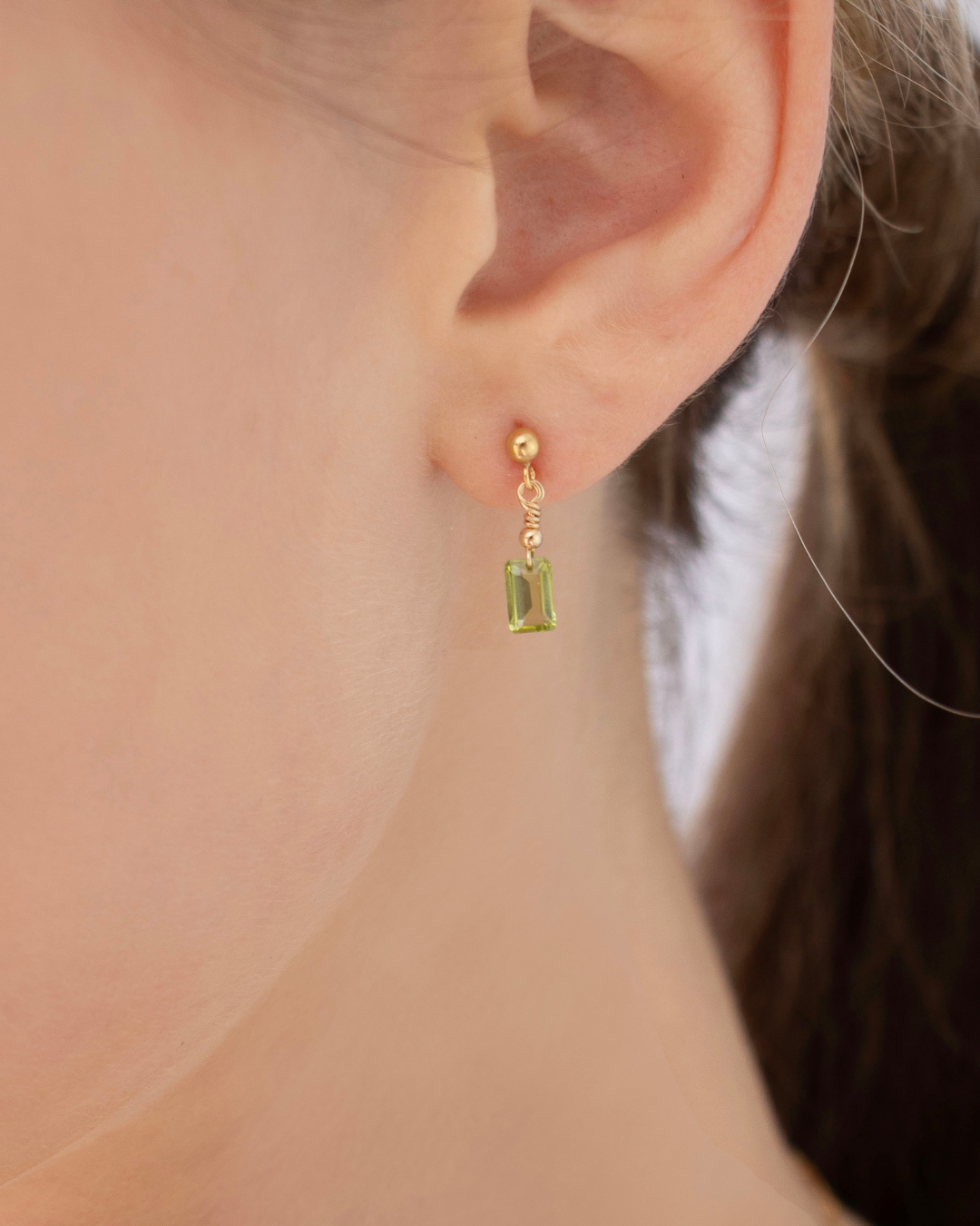 Close-up of a woman's ear wearing a gold peridot stud drop earring 