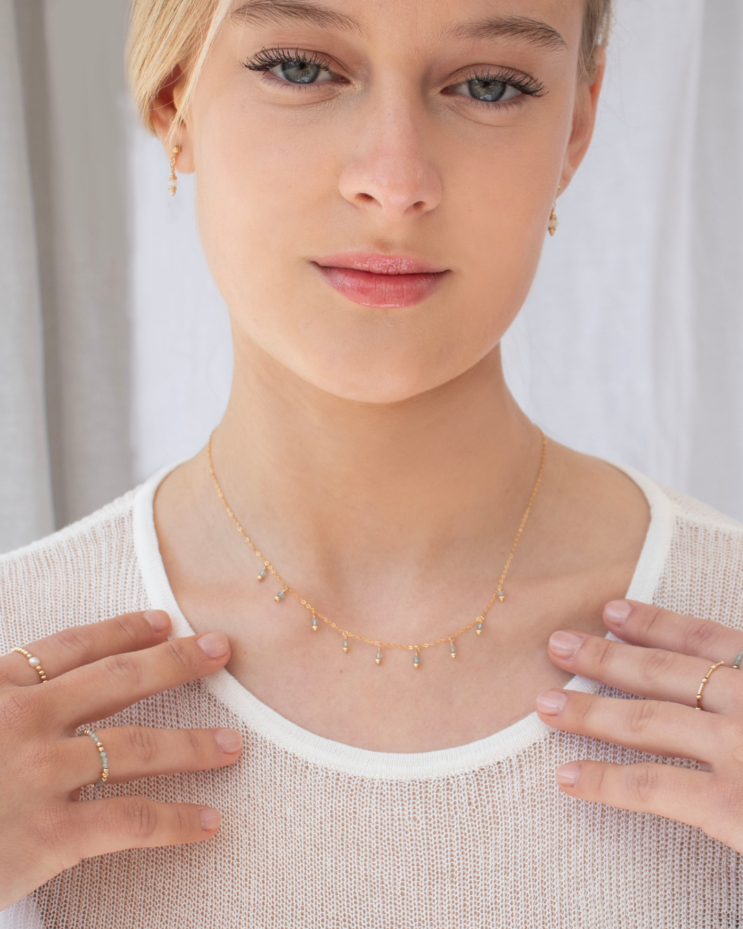 Woman wearing a delicate gold apatite gemstone necklace, gold bead rings and opal earrings