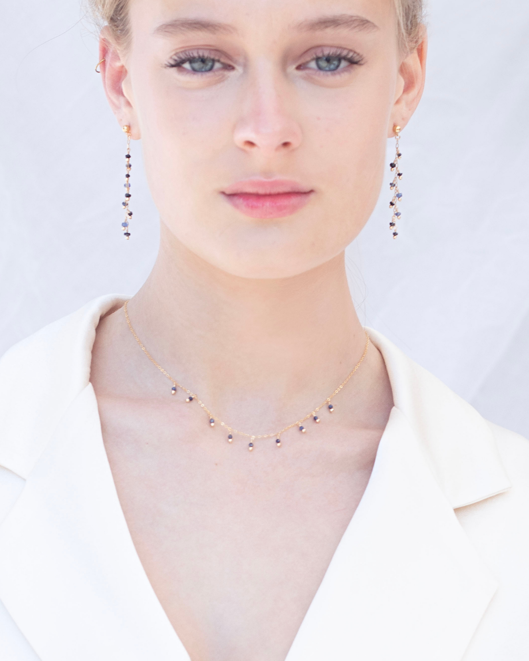 Close-up of a woman wearing a sapphire necklace and earrings on a light background