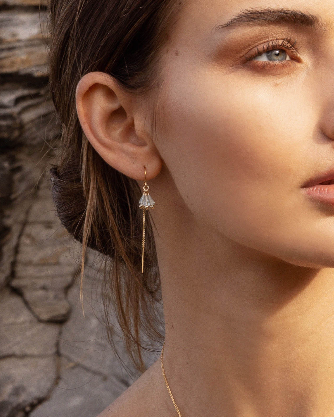 Close-up of a woman wearing a gold thread aquamarine gemstones earring with a stone wall background