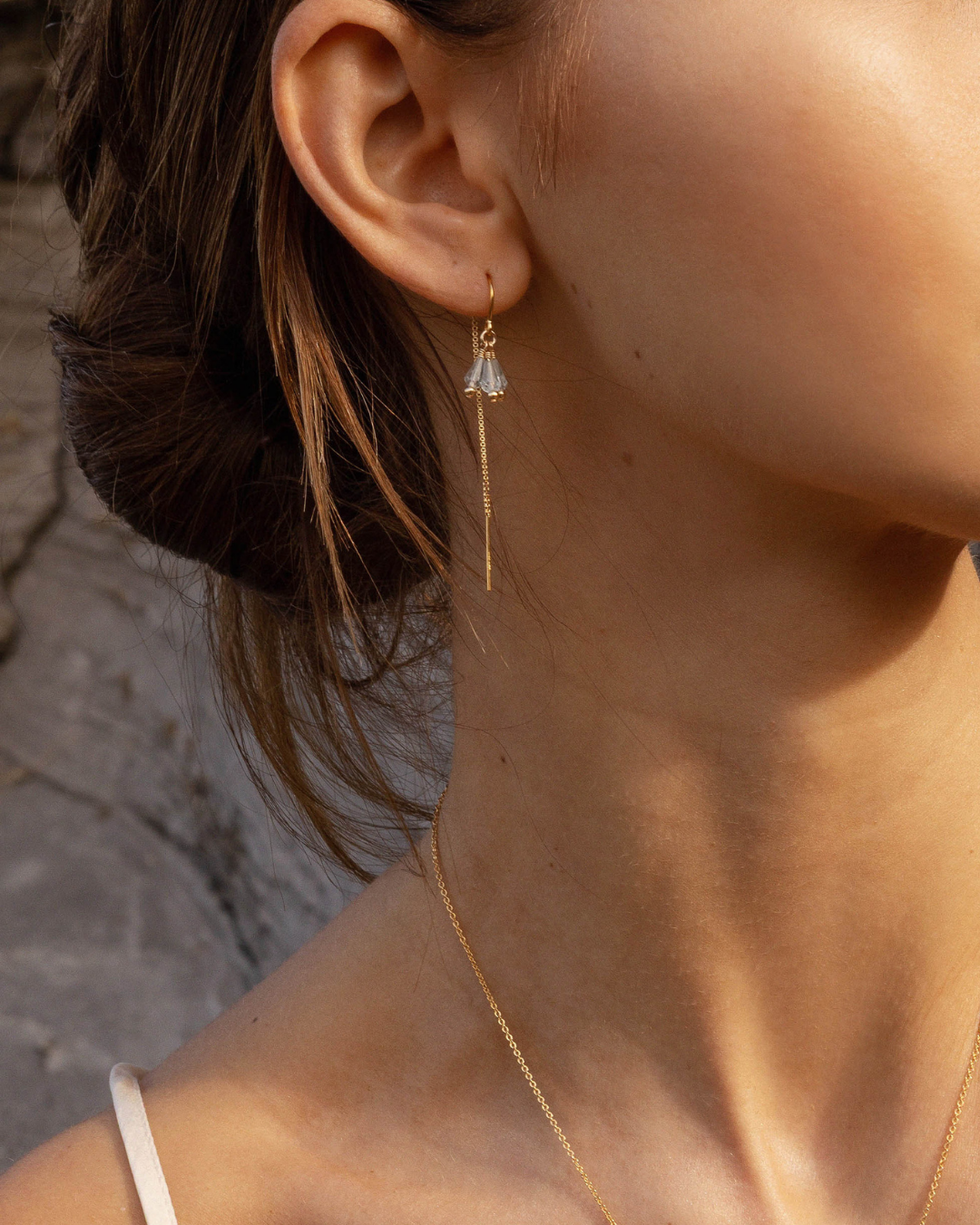 Close-up of a person wearing a delicate gold earring with a blue aquamarine gemstones against a neutral background.
