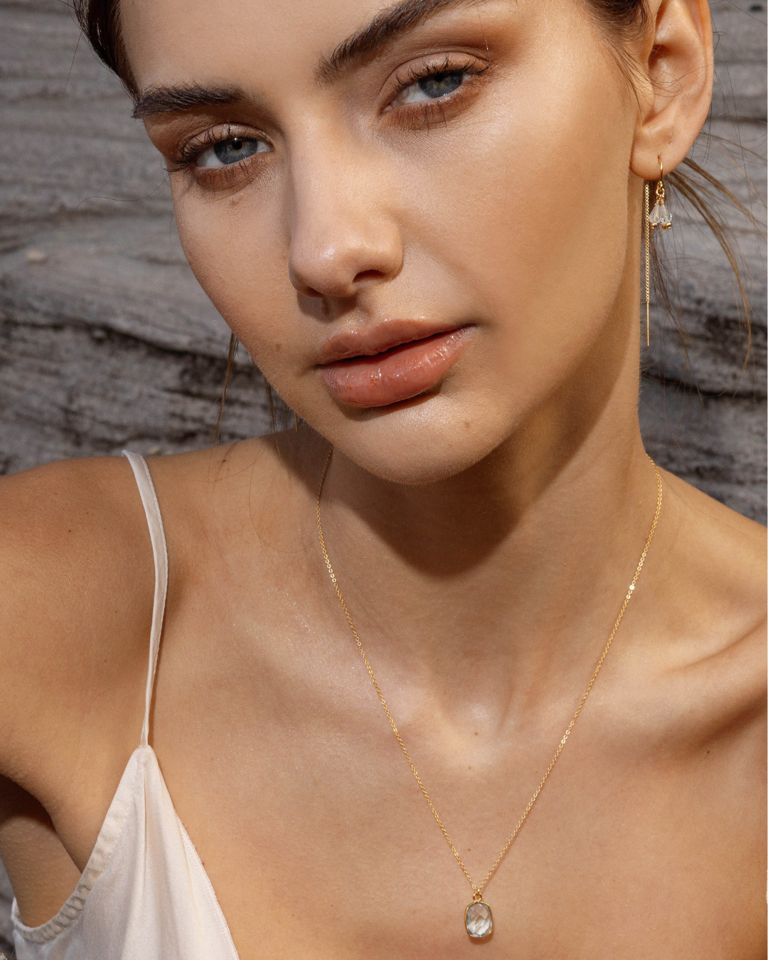 Woman wearing gold thread aquamarine earrings and a gold chain necklace with a blue topaz pendant