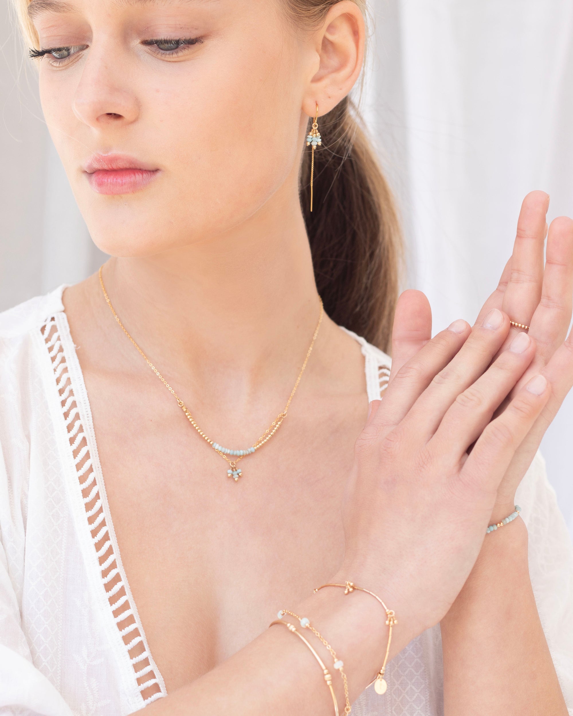 Woman wearing gold larimar jewellery including a necklace, earrings, and bracelets on a white background