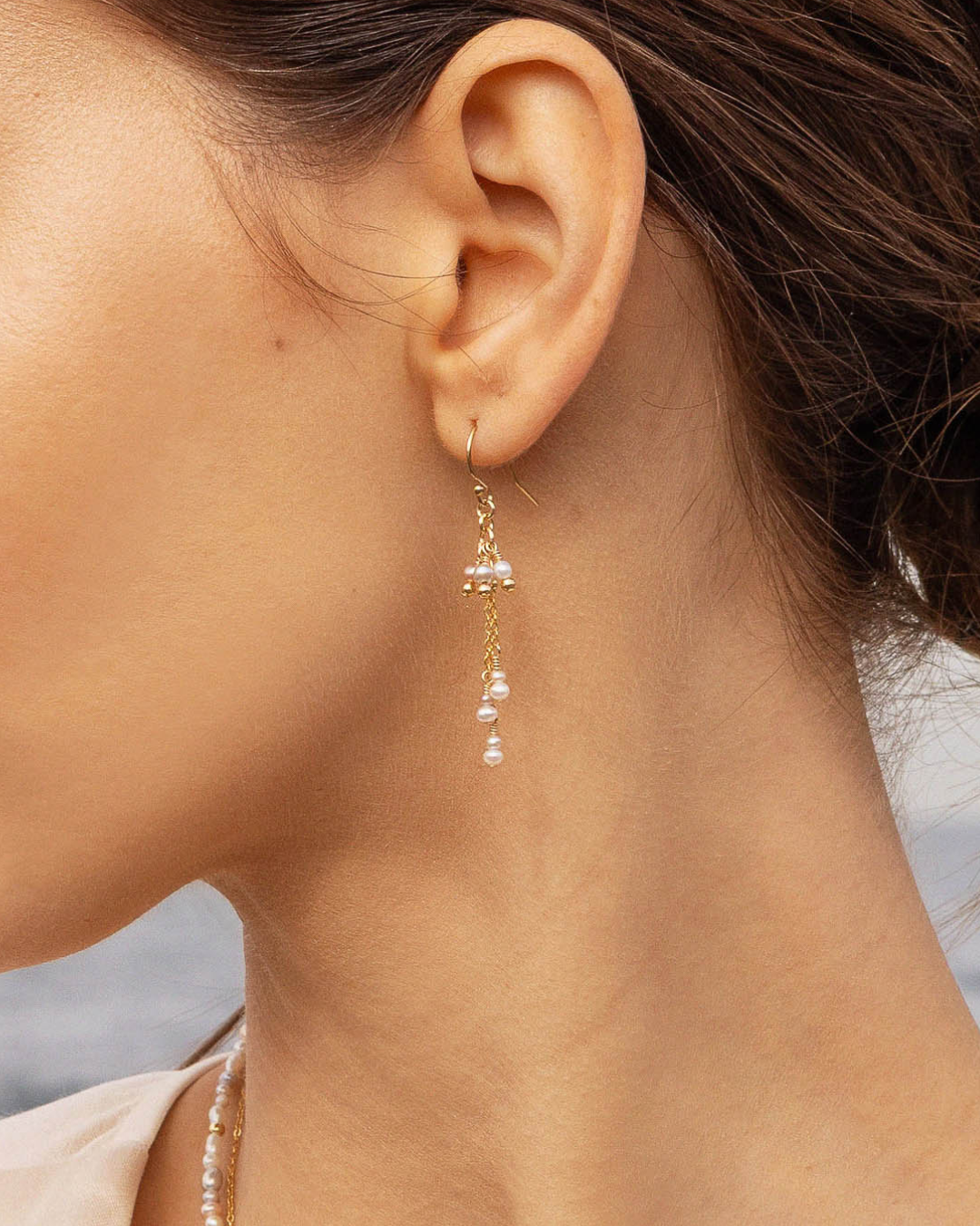 Close-up of a woman's ear wearing a gold pearl drop earring