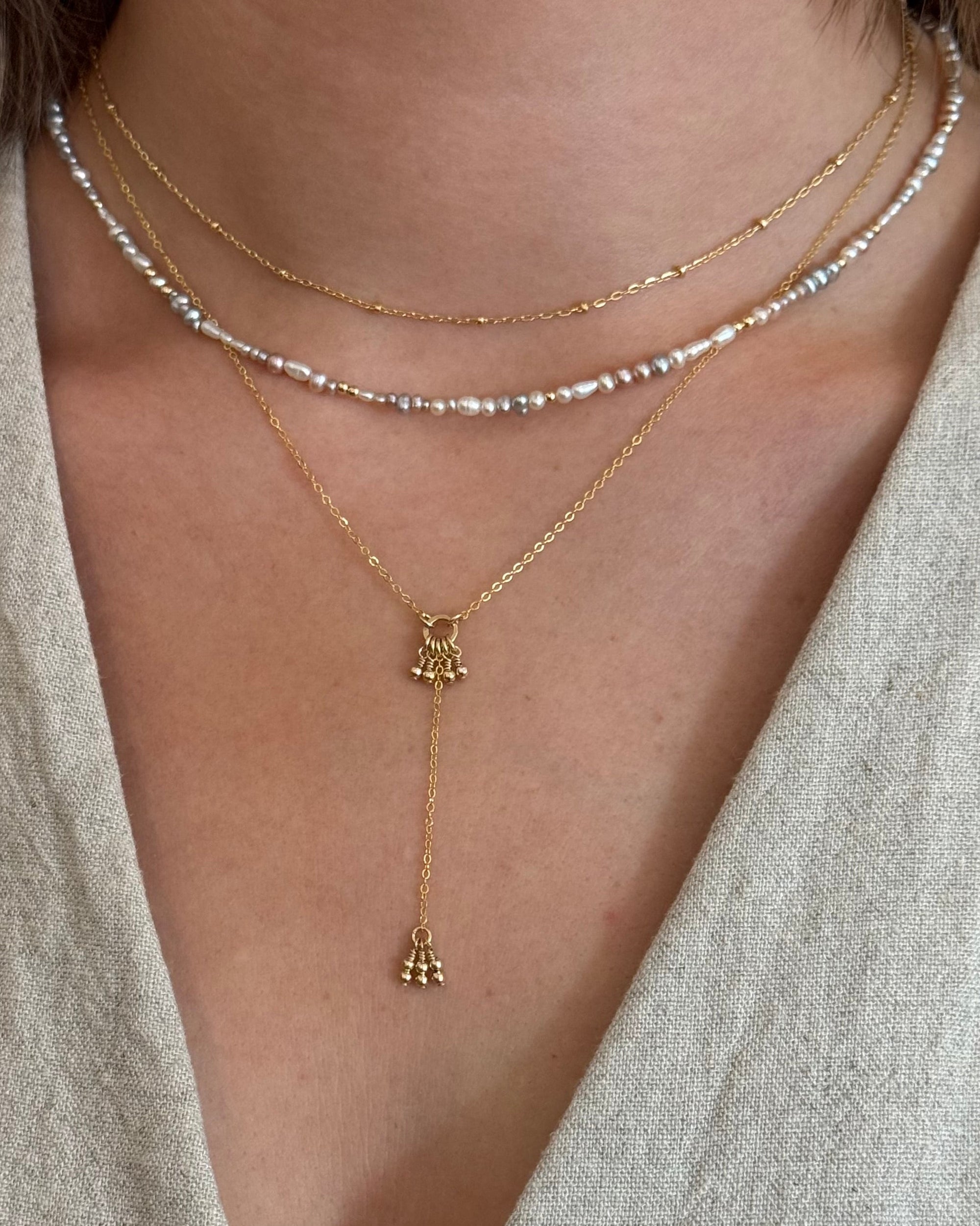 Close-up of a woman wearing layered gold necklaces with a pearl and gold beaded necklace