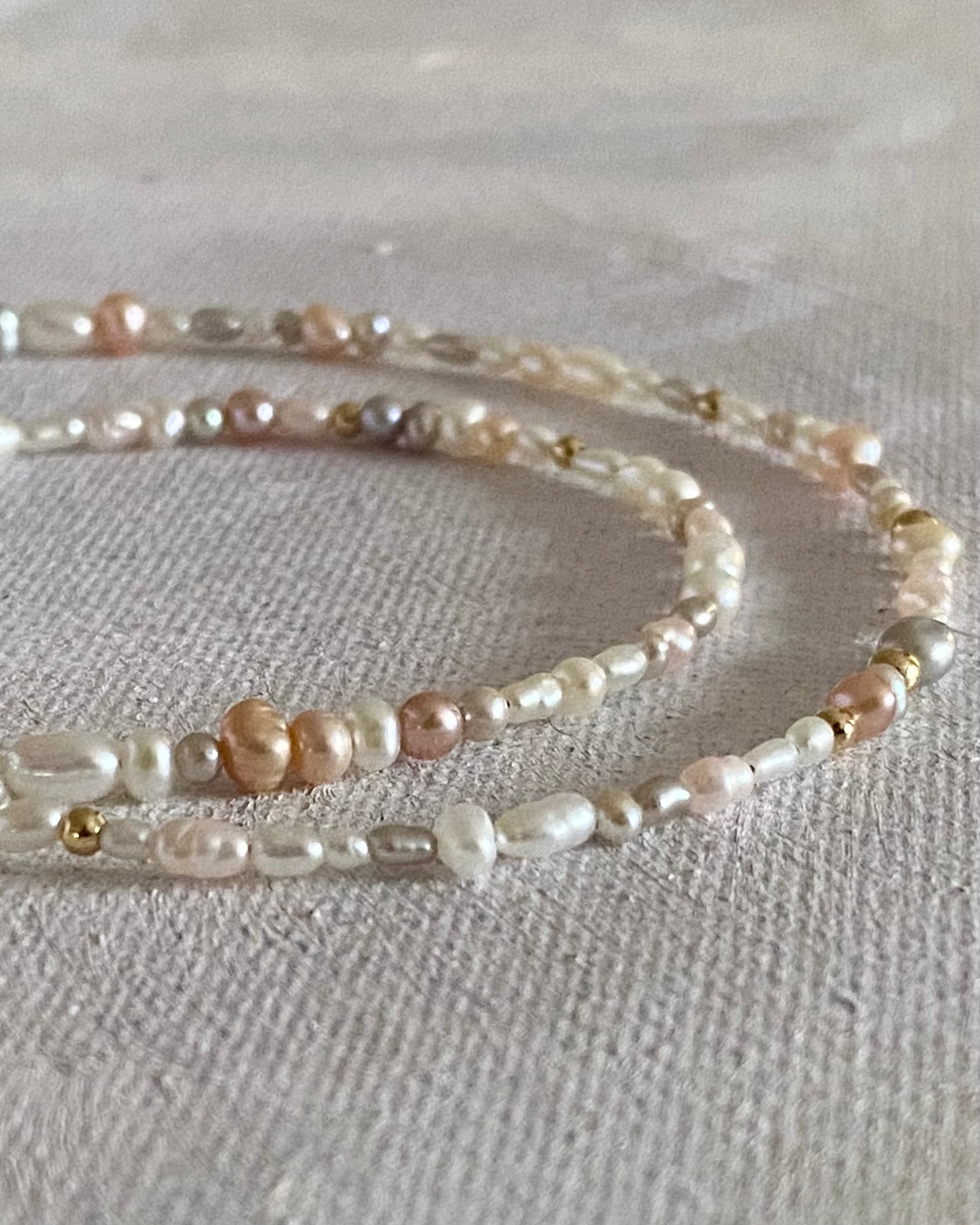 Close-up of a pearl gold beaded necklace pearl on a textured beige surface