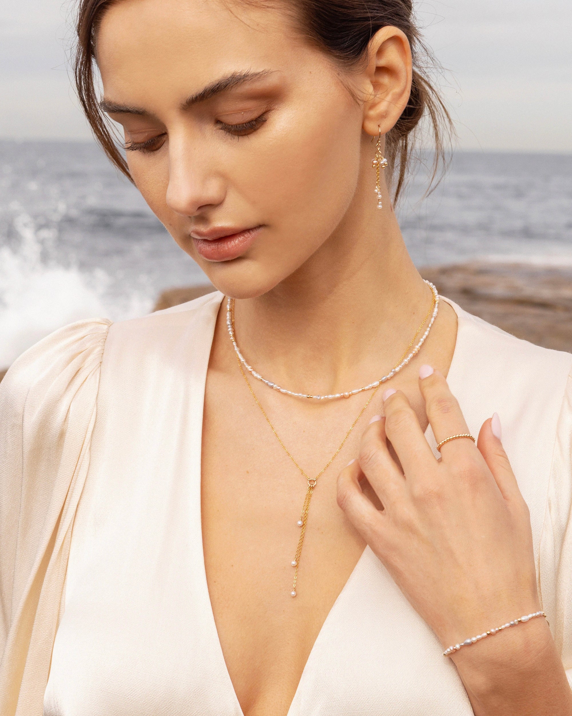 Woman wearing layered  pearl necklaces, earrings, ring, and bracelet by the ocean