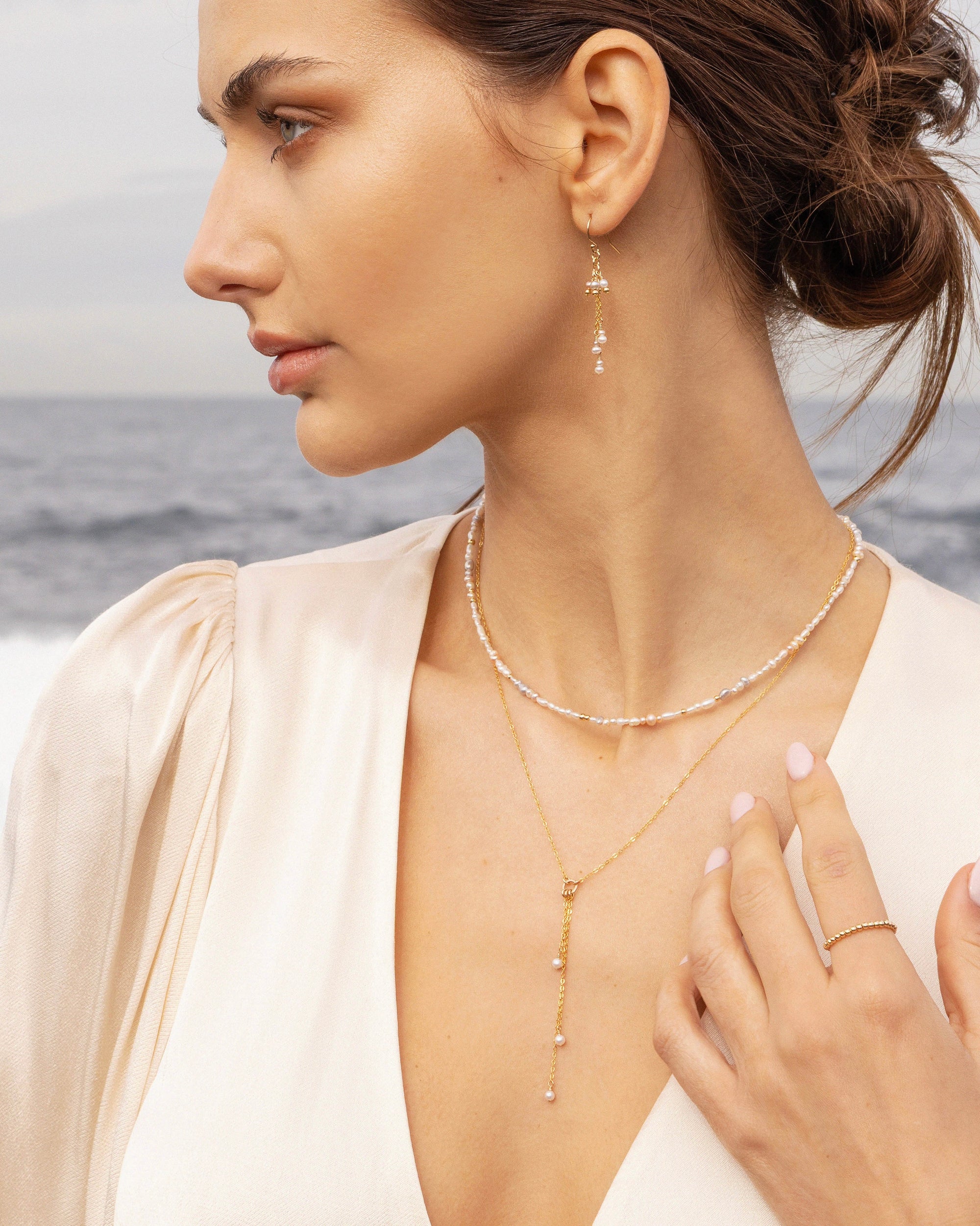 Woman wearing gold pearl jewellery with a blurred ocean background