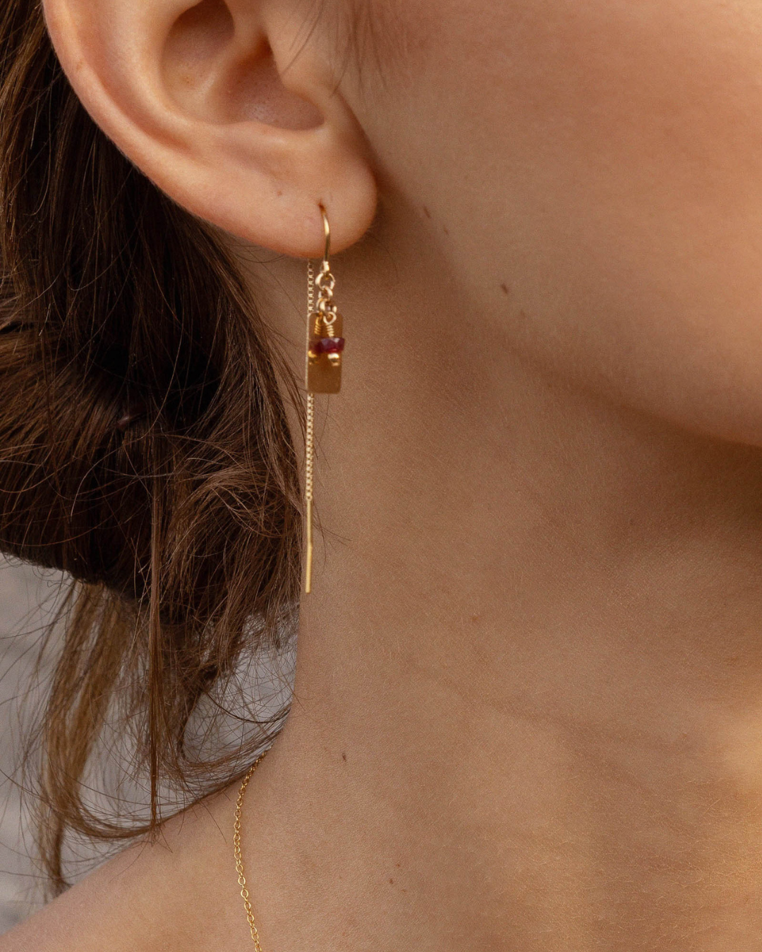 Close up of a womam's ear with a gold thread ruby earring