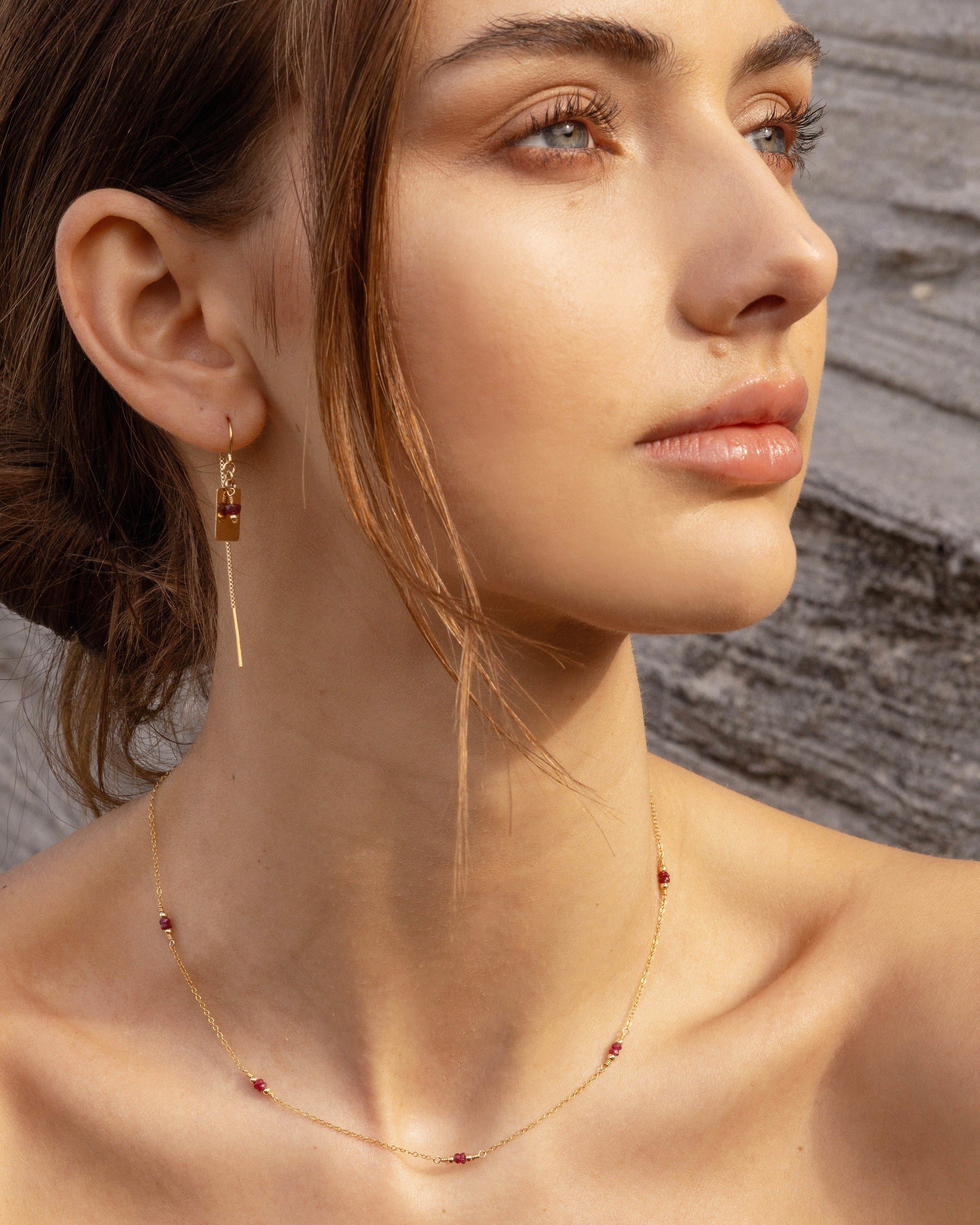 Close-up of a woman wearing gold ruby thread earrings and ruby necklace against a neutral background