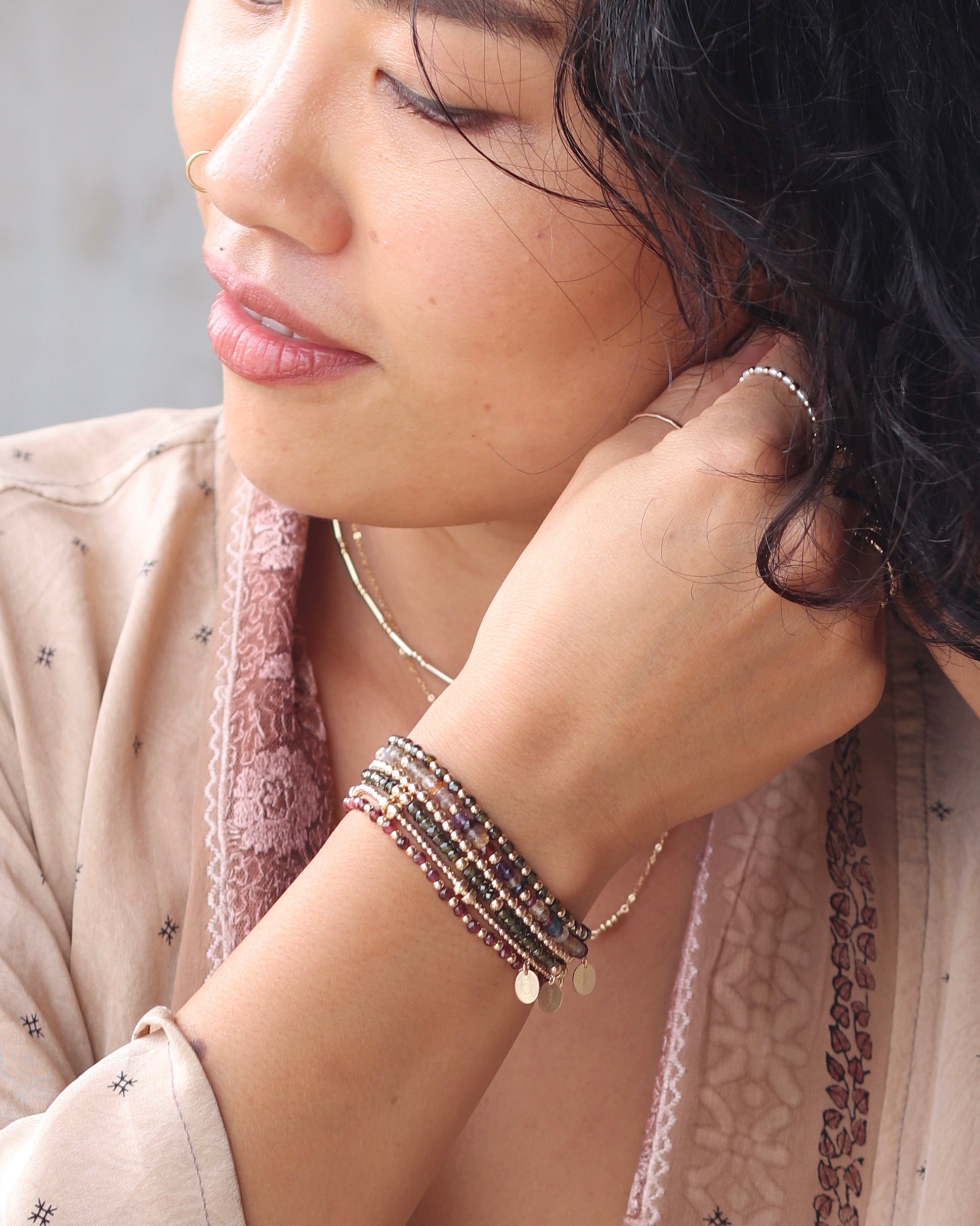 Woman in a silk top wearing multiple gold gemstone bracelets, necklace, and rings