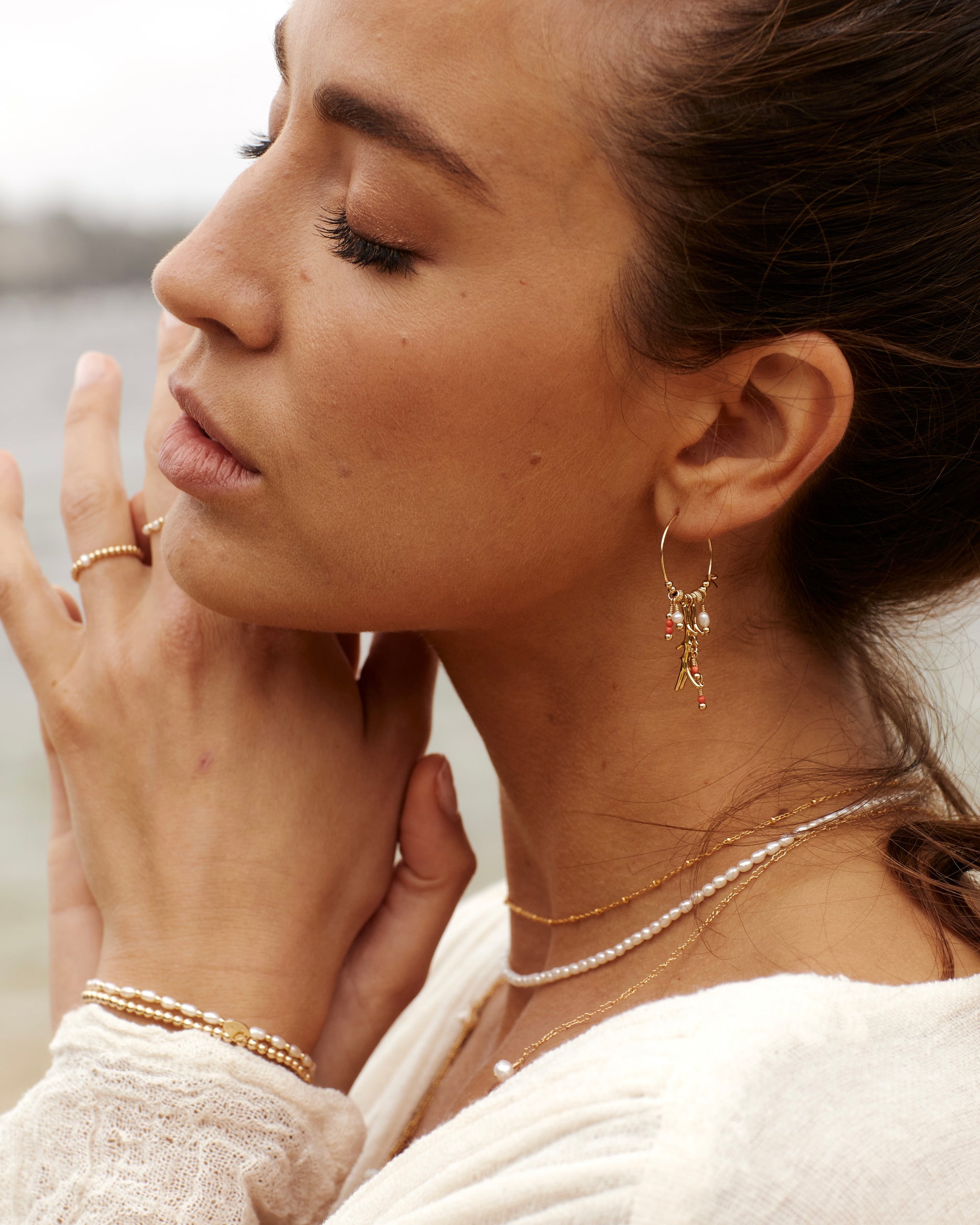 Close-up of a woman wearing gold pearl jewellery with a blurred natural background