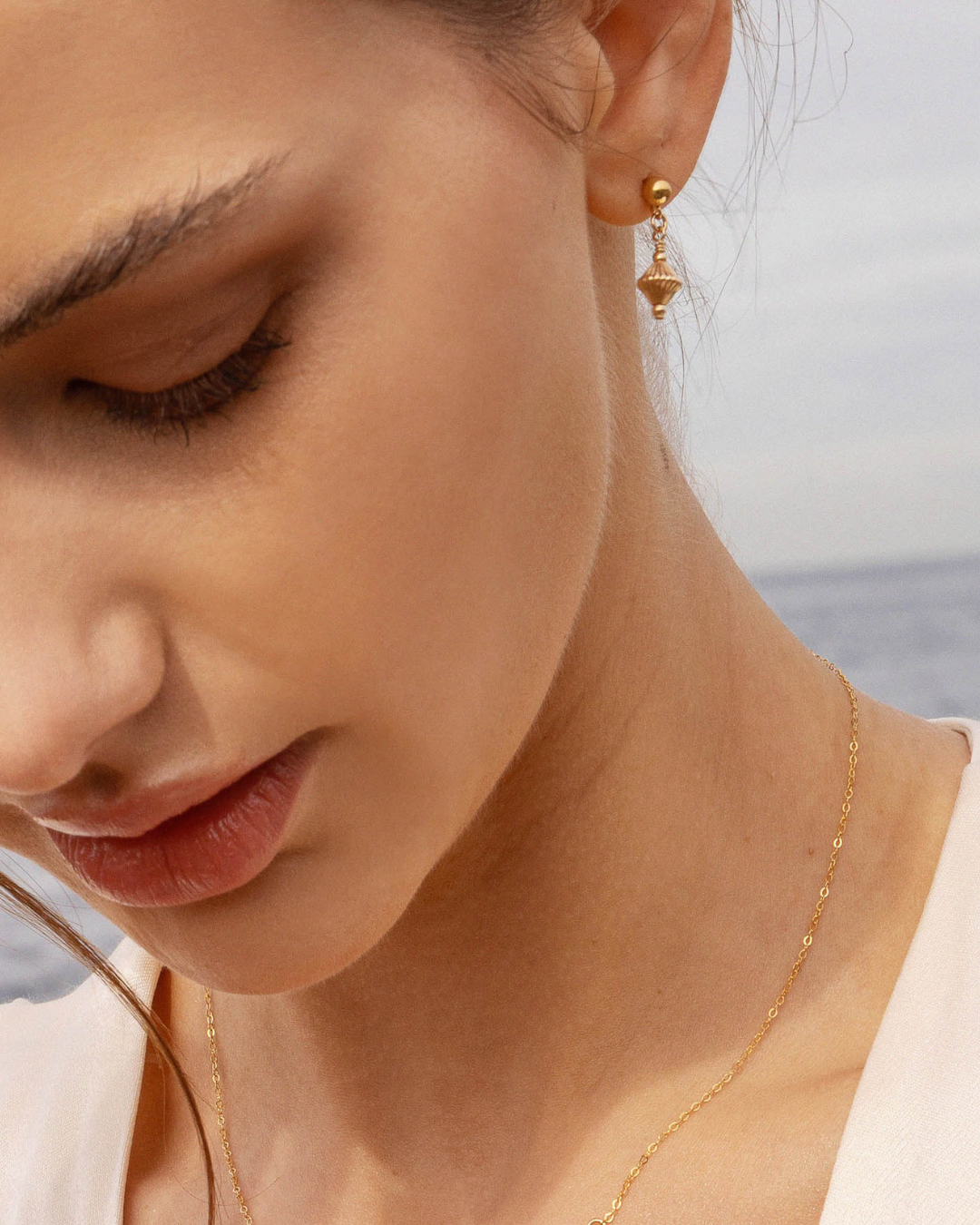 Close-up of a woman wearing a gold stud drop earring