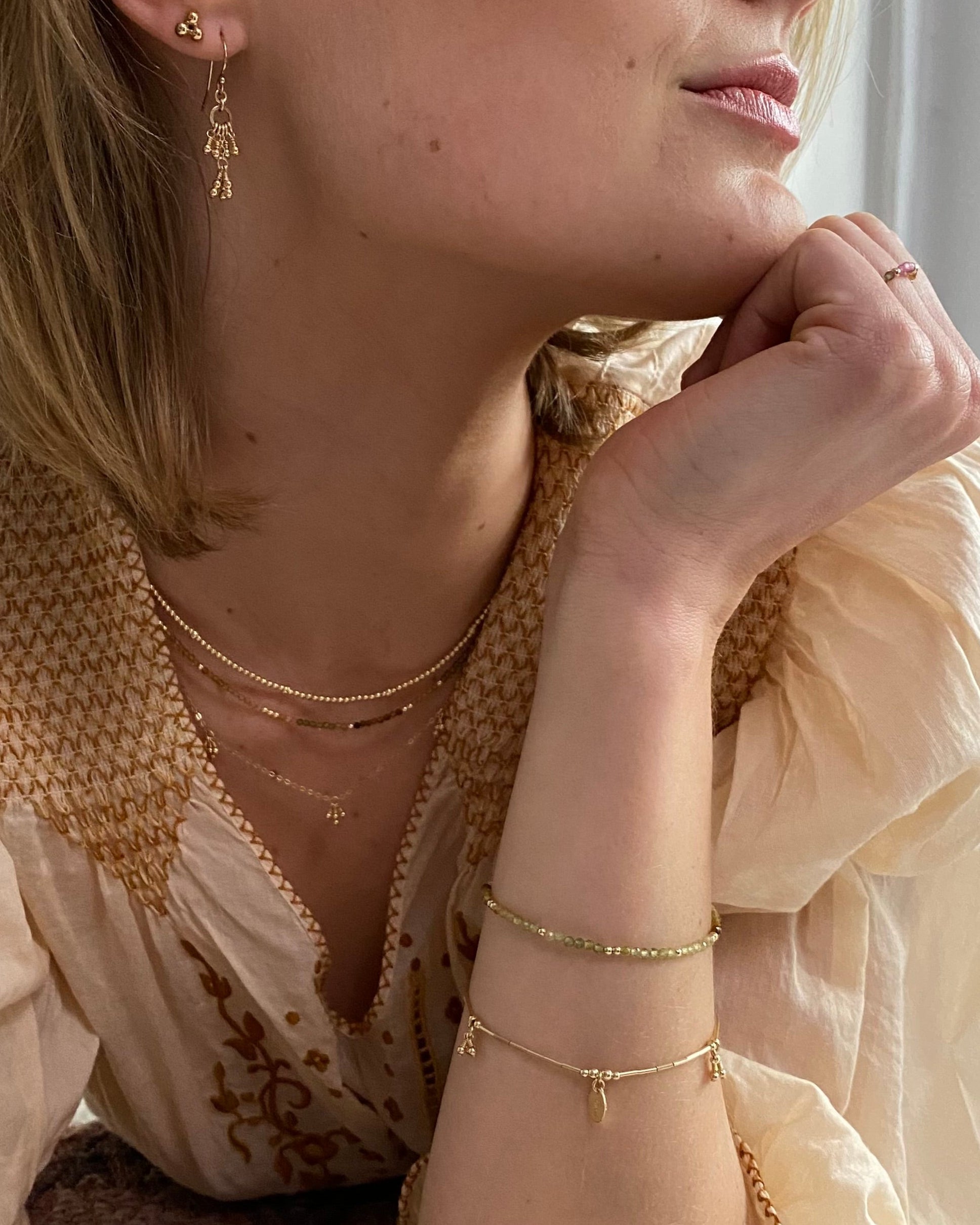 Close-up of a woman wearing gold earrings, tourmaline gemstone necklace and bracelet layered with gold necklaces.