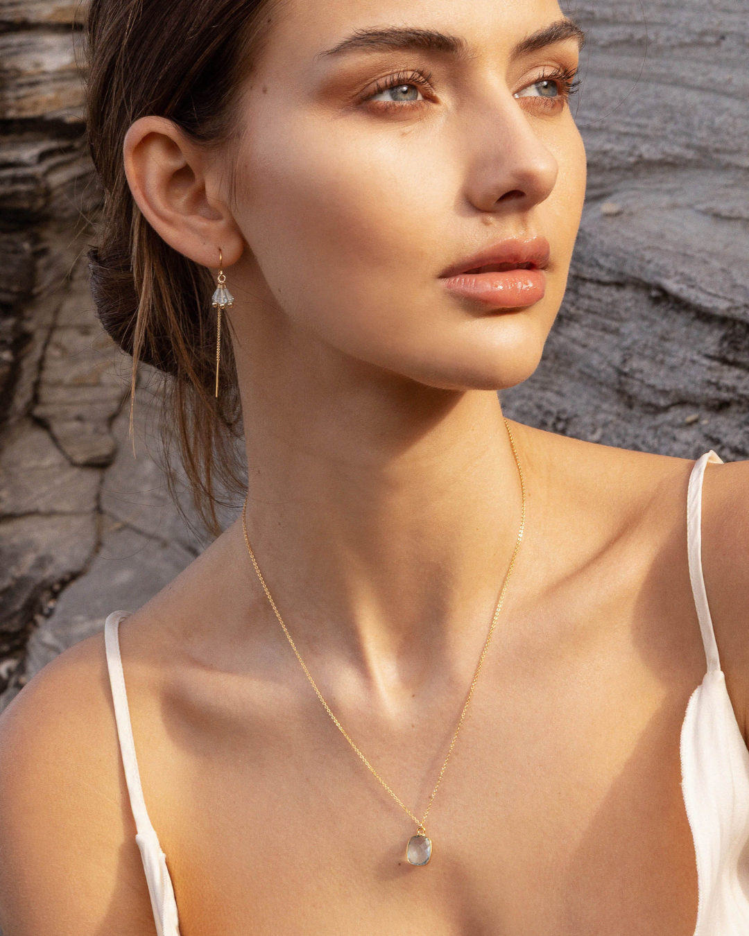 Woman wearing a gold necklace with a stone pendant against a stone wall background