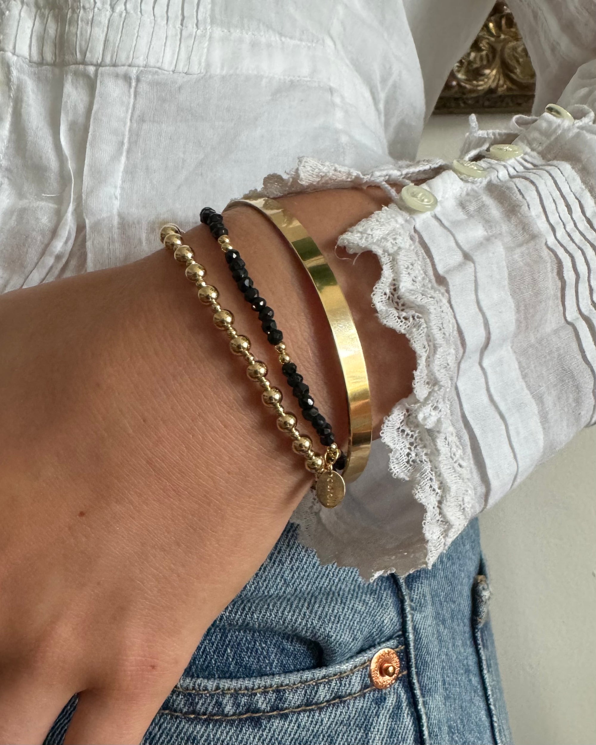 Close-up of a woman wearing a white lace top and jeans with gold and gemstone bracelets