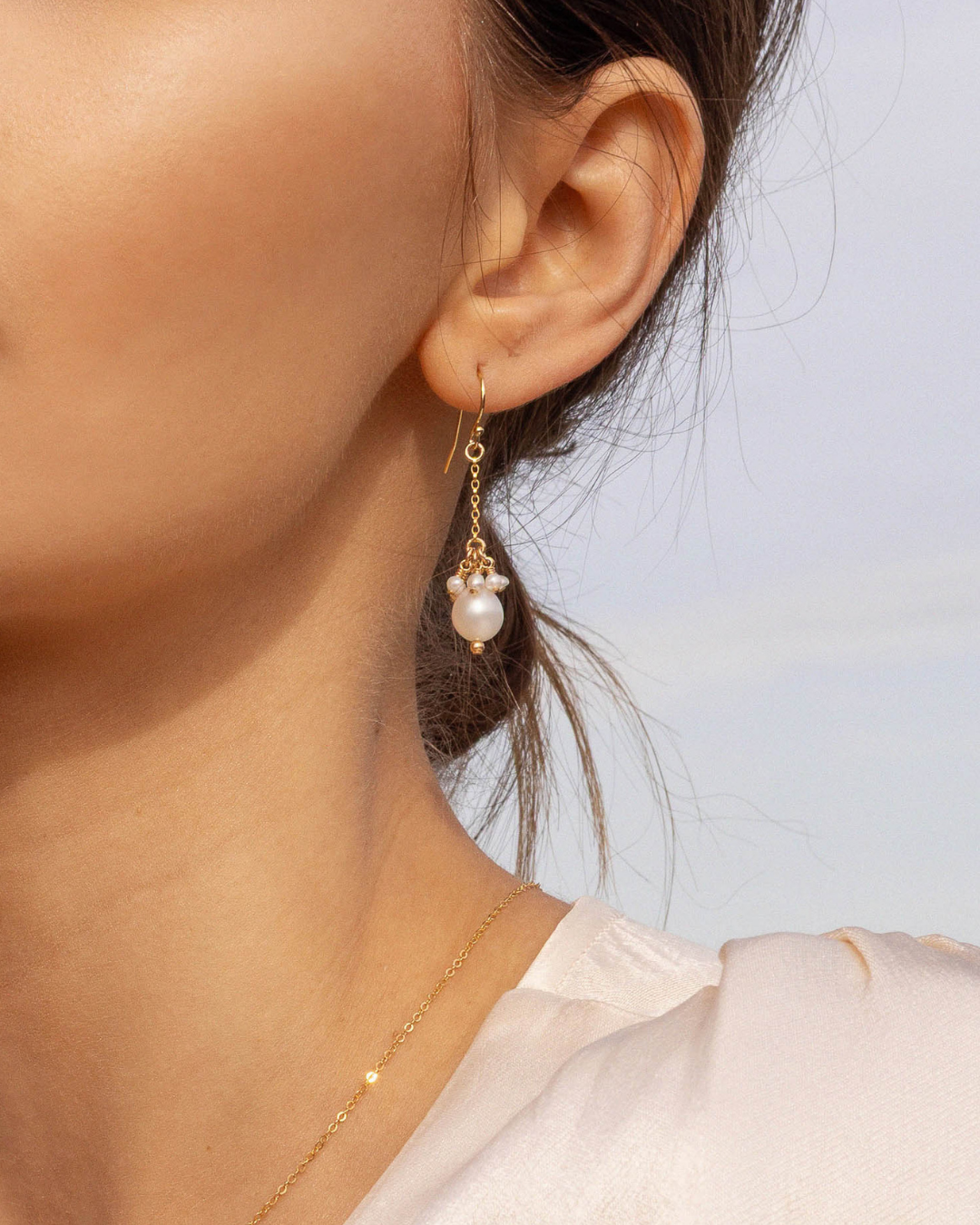 Close-up of a woman wearing a gold pearl drop earring against a light background