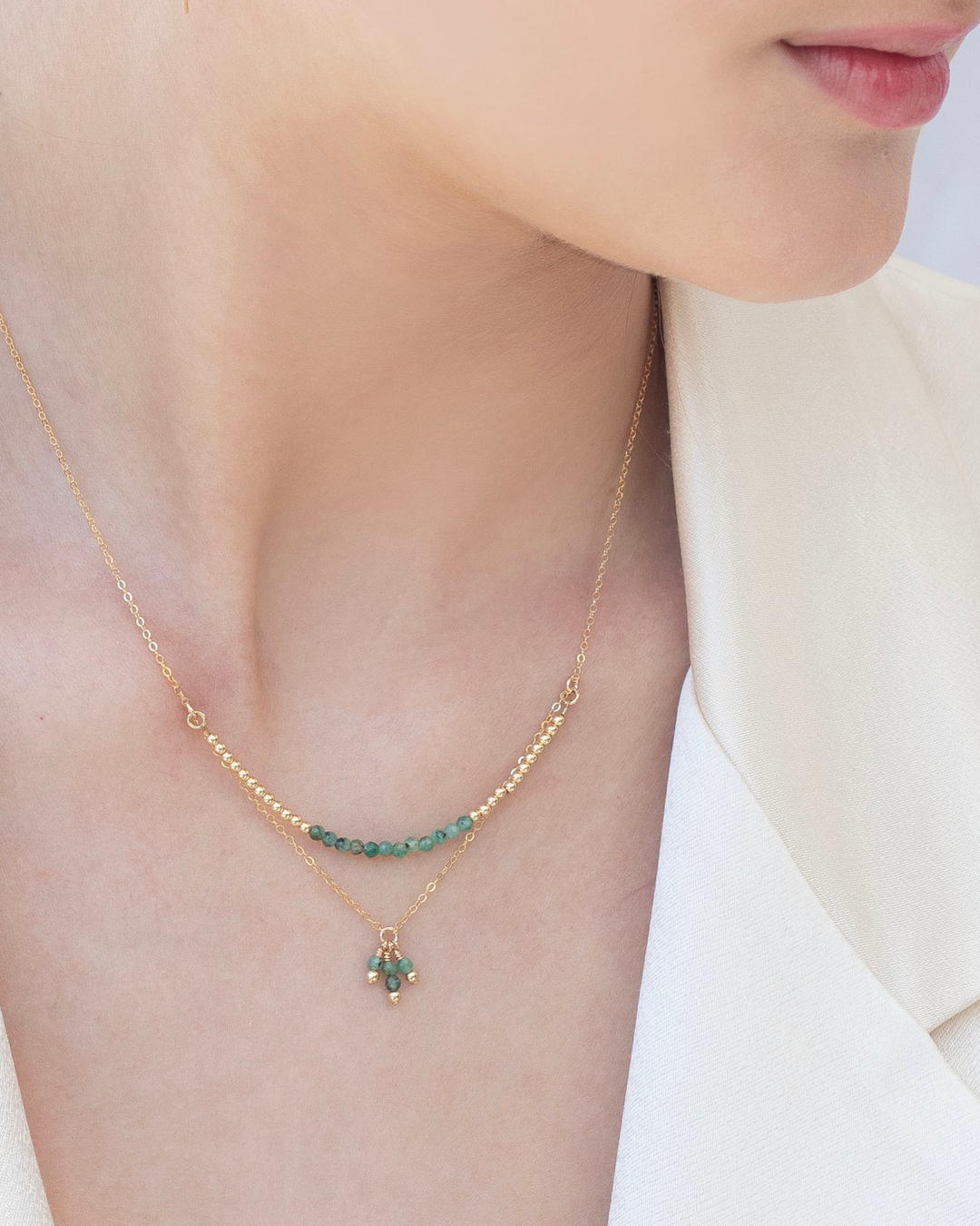 Close up of a woman's neck wearing a gold emerald necklace