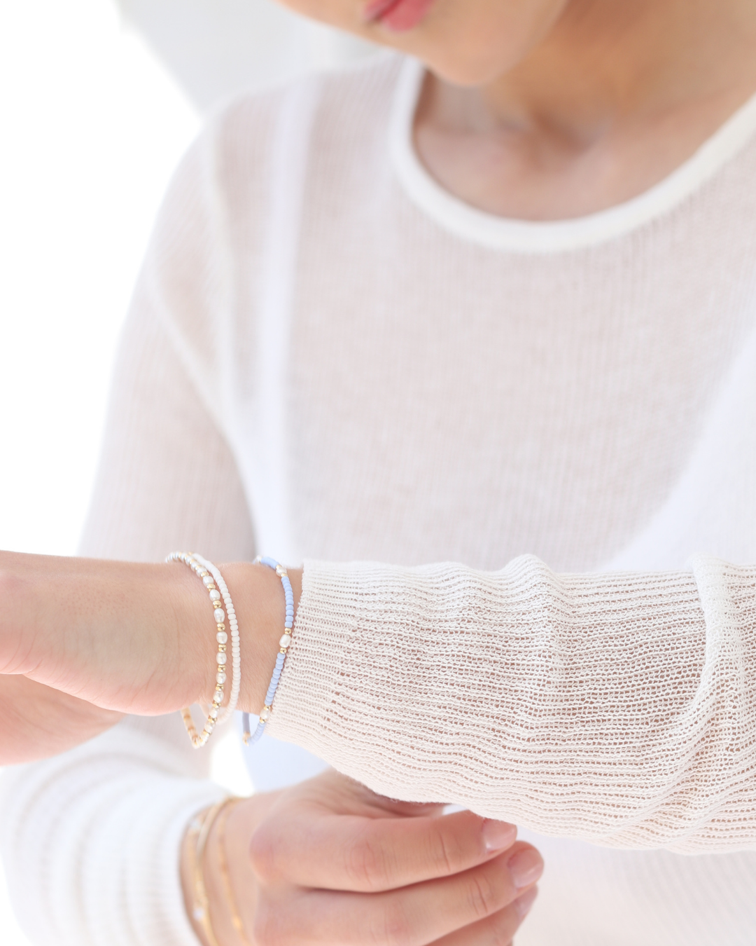 Close-up of a woman wearing multiple bracelets featuring pearls wearing a fine white jumper.