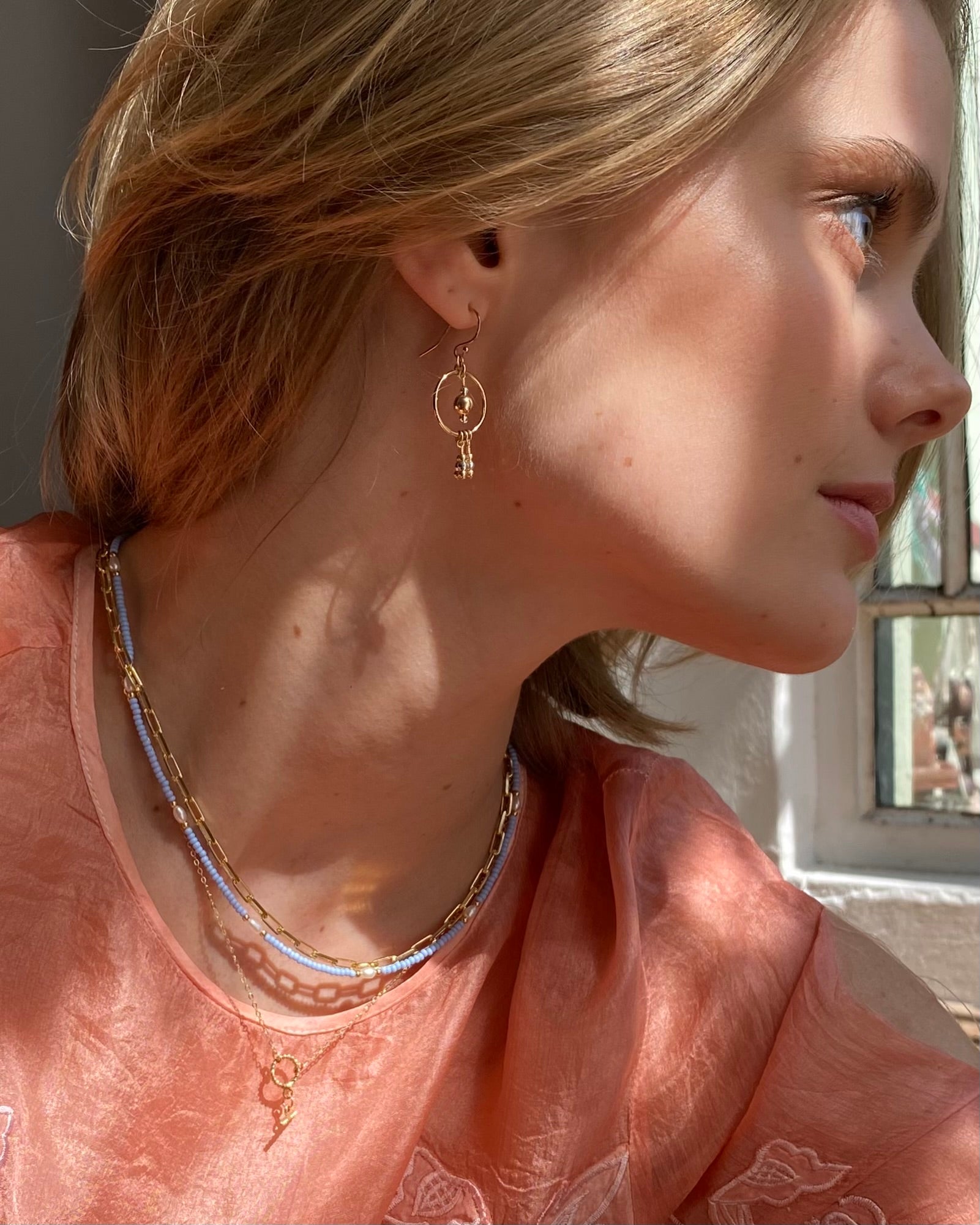 Close-up of a woman wearing gold drop earrings and layered necklaces.