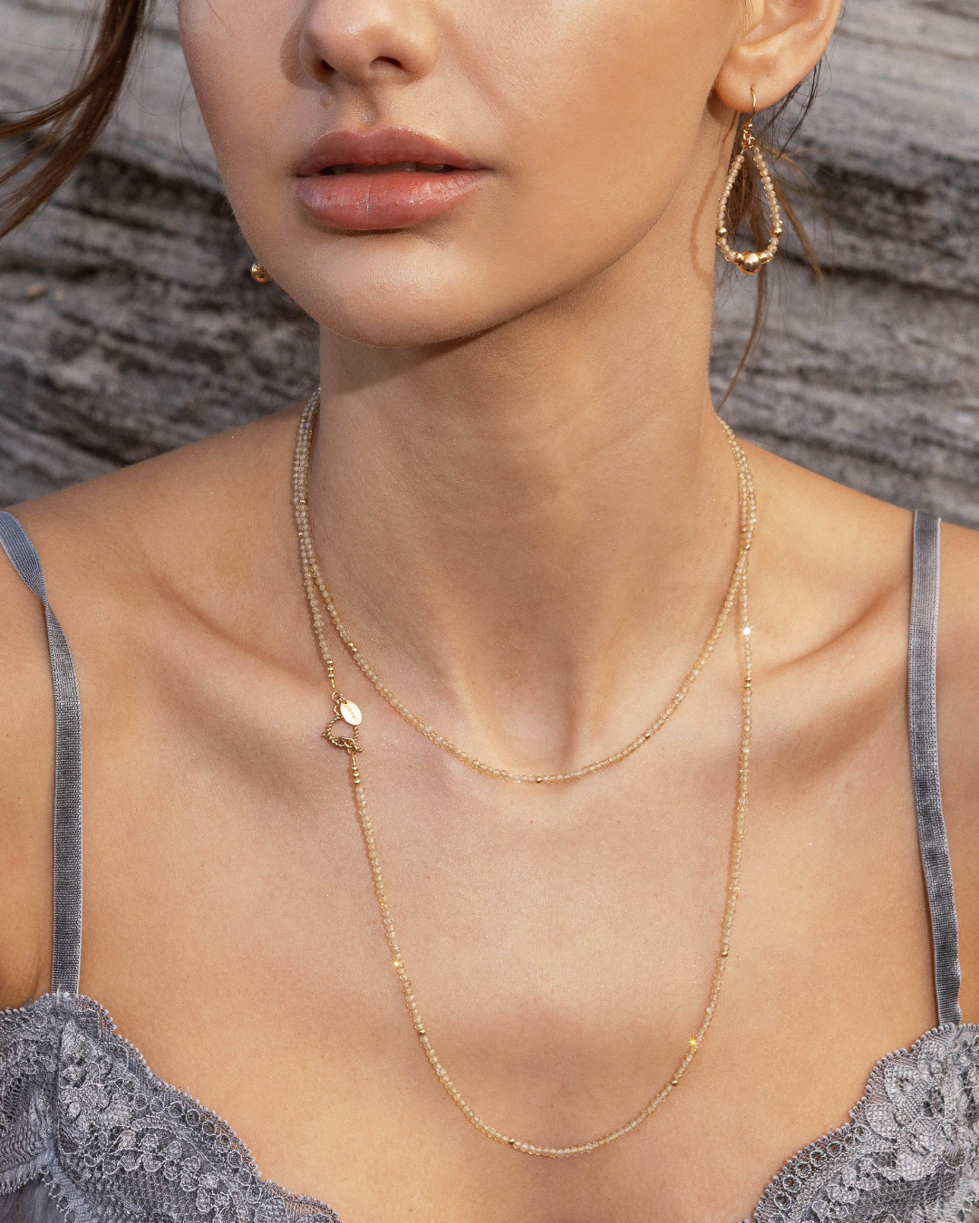 Close up of a model in a grey silk singlet top wearing a zircon gemstone necklace with matching earrings