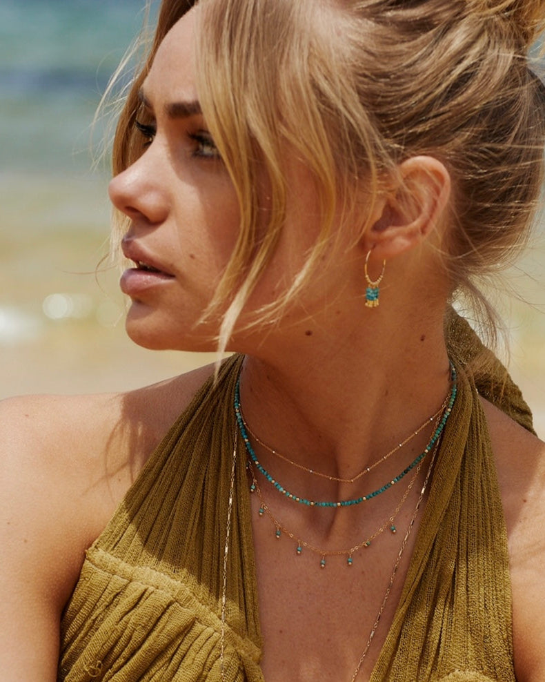 Woman wearing layered gold and turquoise earrings and necklaces