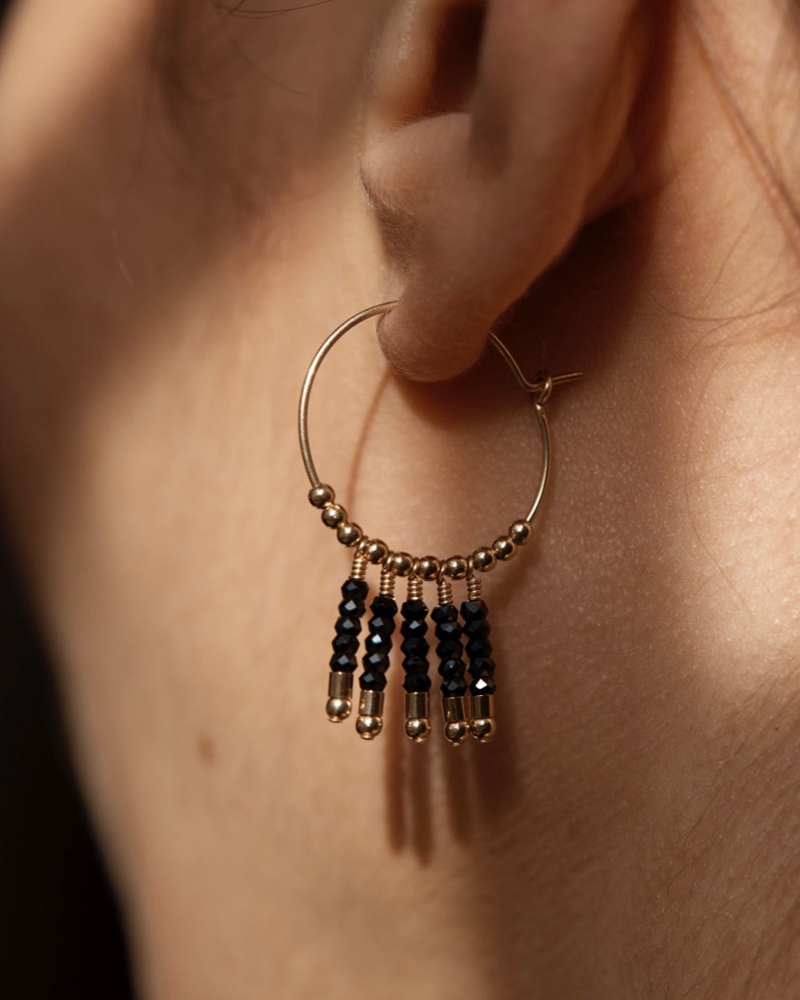 Gold and black spinel hoop earring with beads worn on an ear