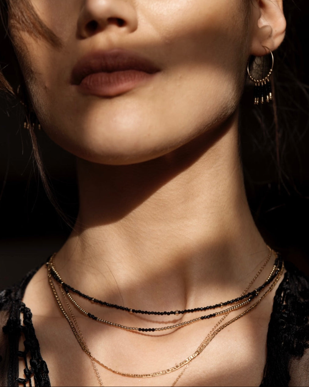 Close-up of a person wearing layered necklaces and hoop earrings with a dark background