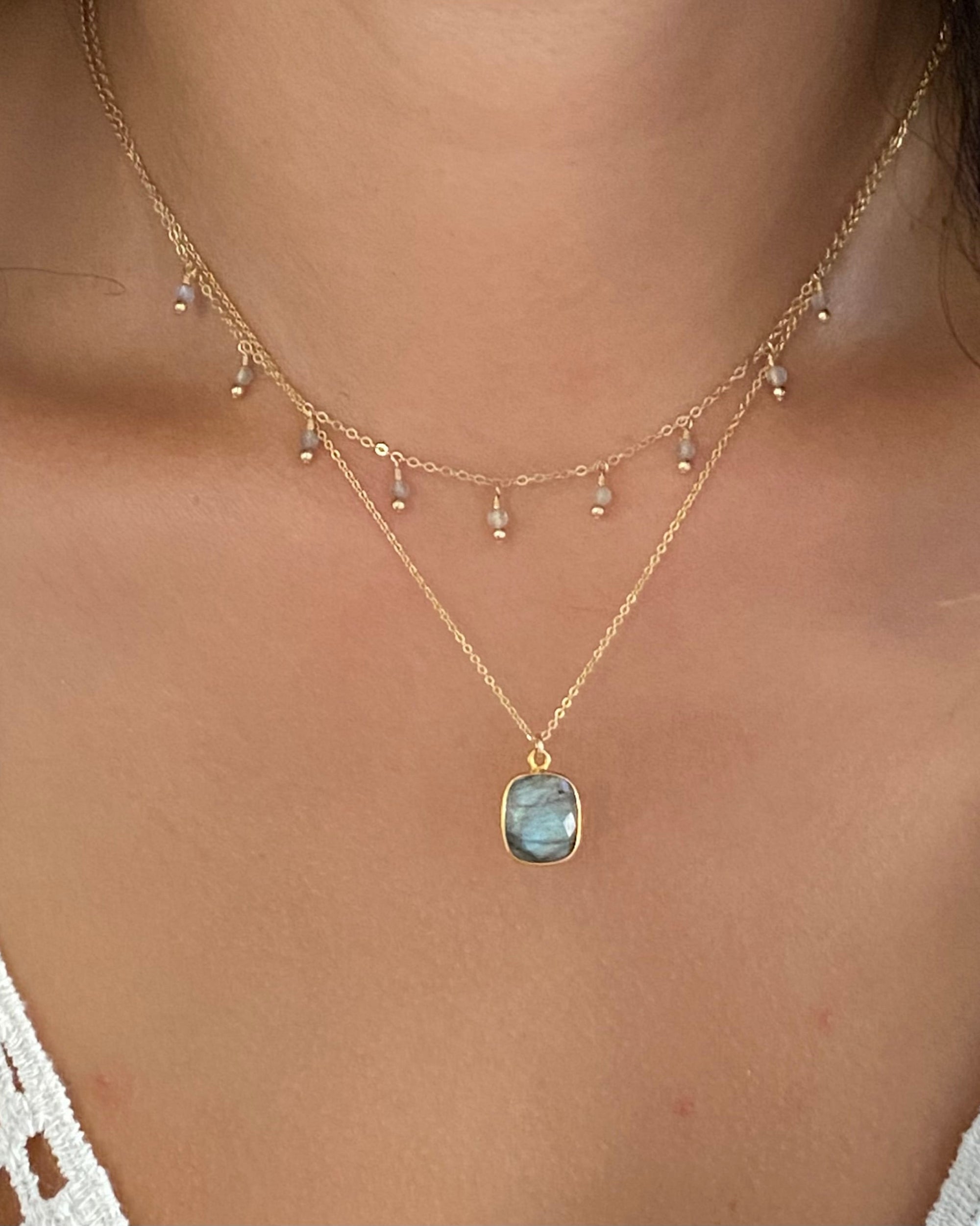 Gold necklace with a labradorite pendant on a person wearing a white lace top.
